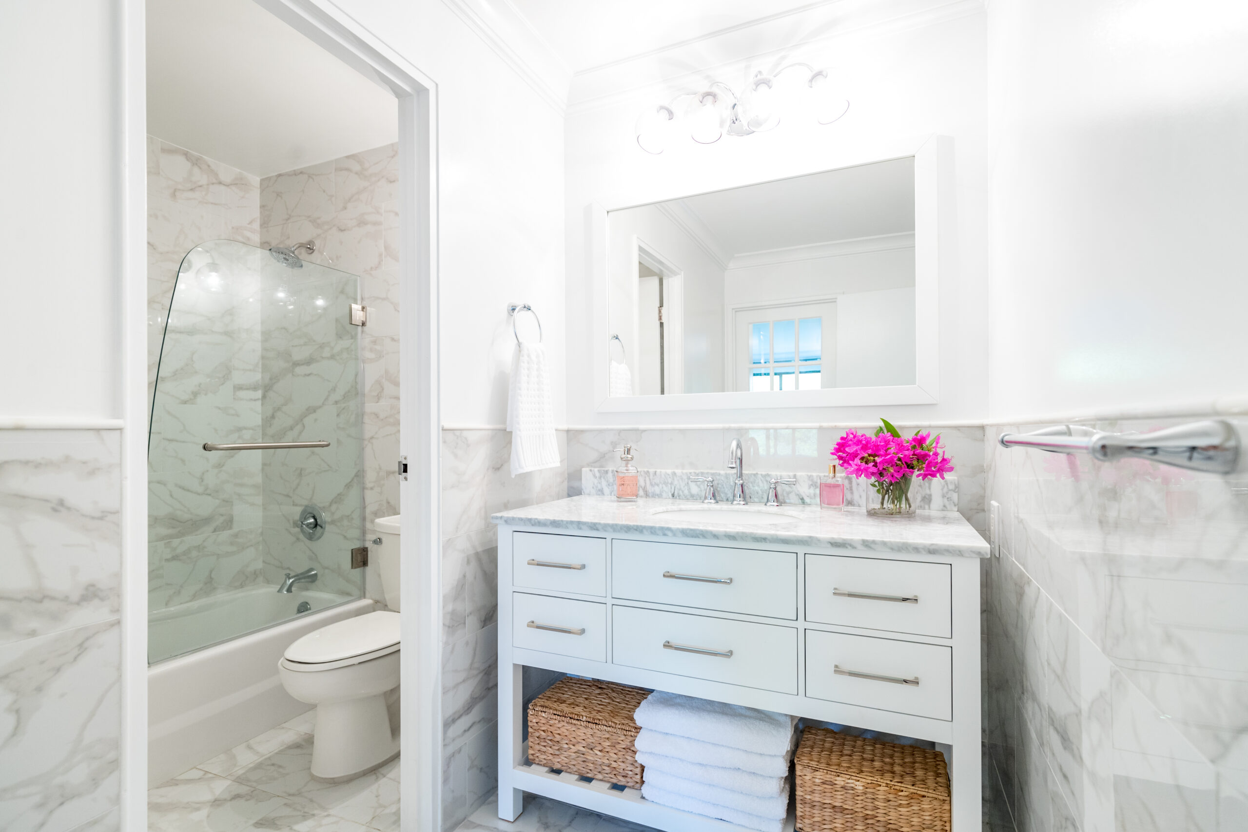 Tatiana’s renovated bathroom with porcelain slab walls, white vanity with sink, and mirror with overhead lighting