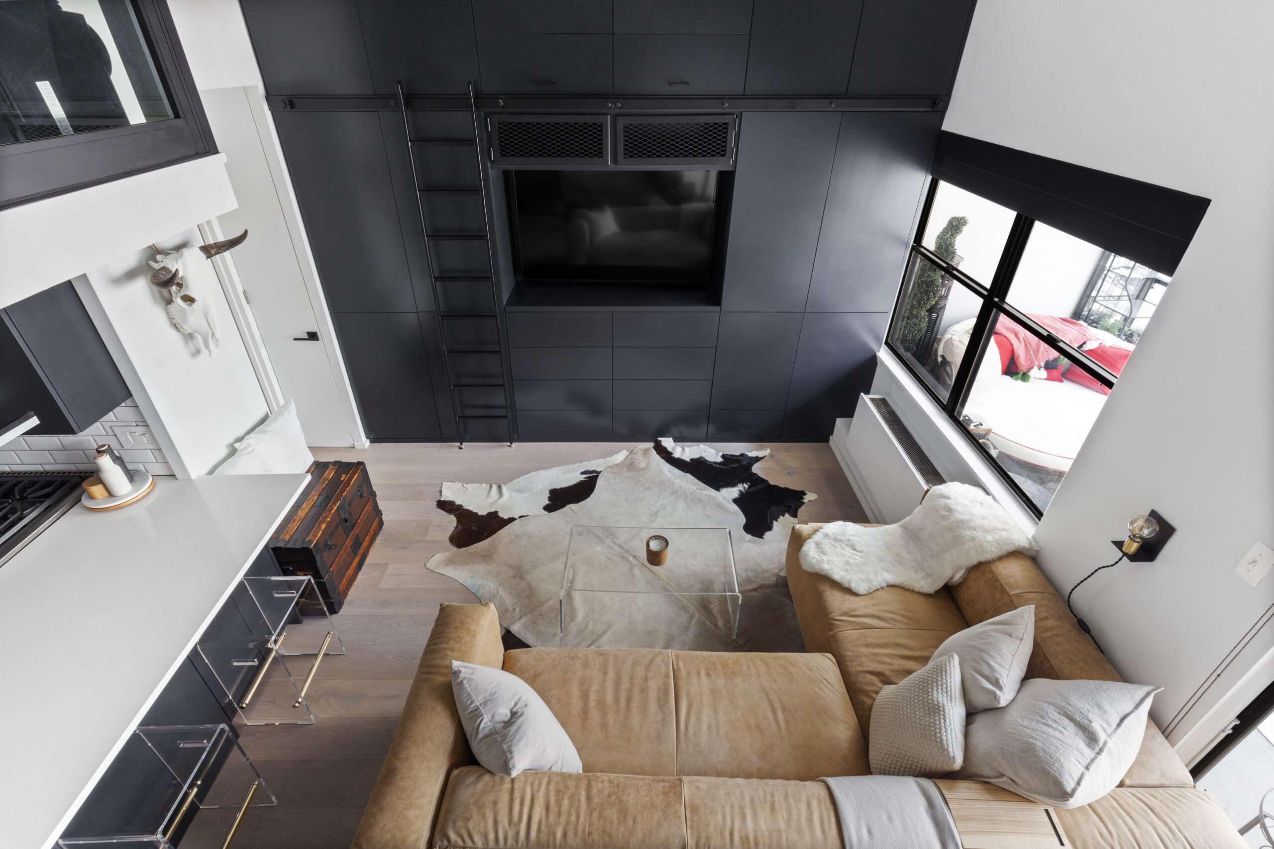 Top view of a studio loft living room with leather couch, TV, rug, and wooden storage chest