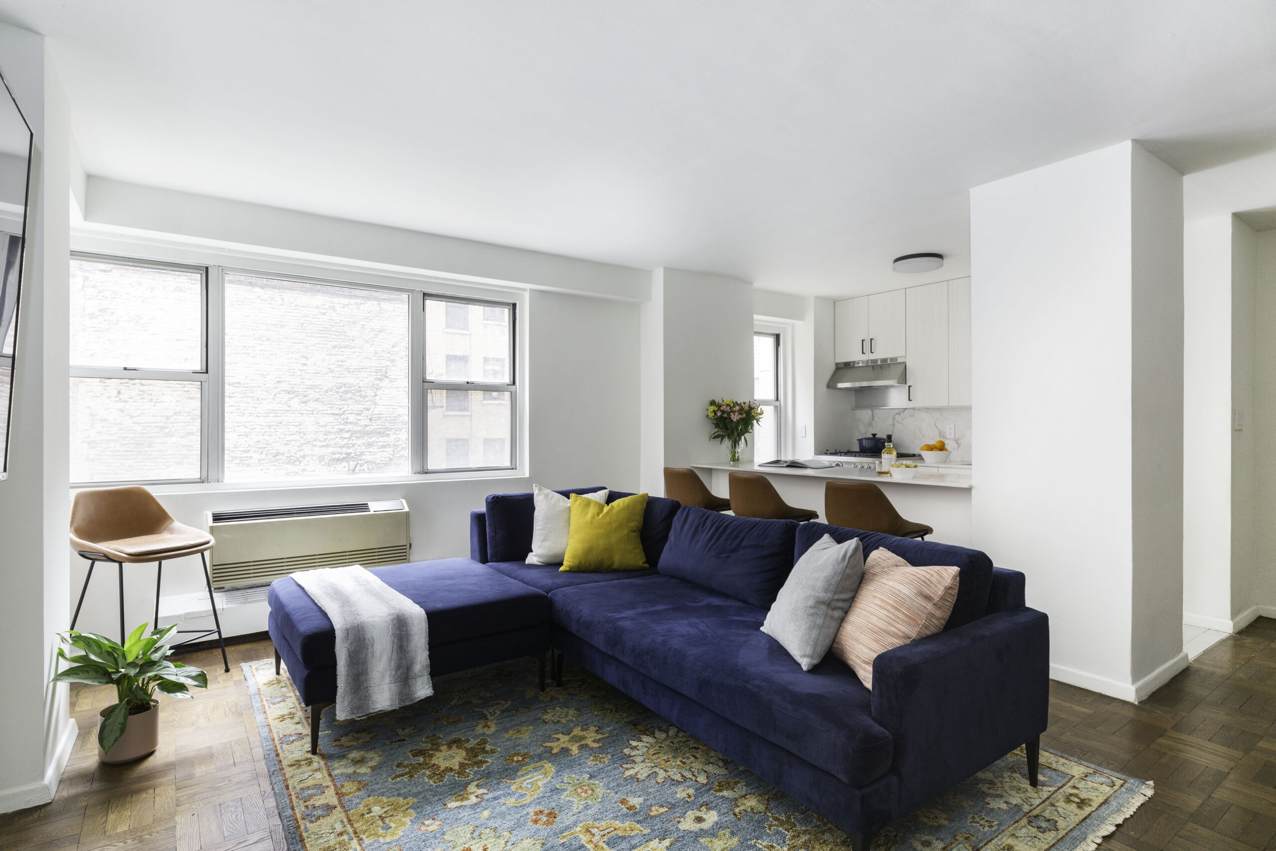 Living room with blue couch and pillows, a rug, with wooden flooring, and windows