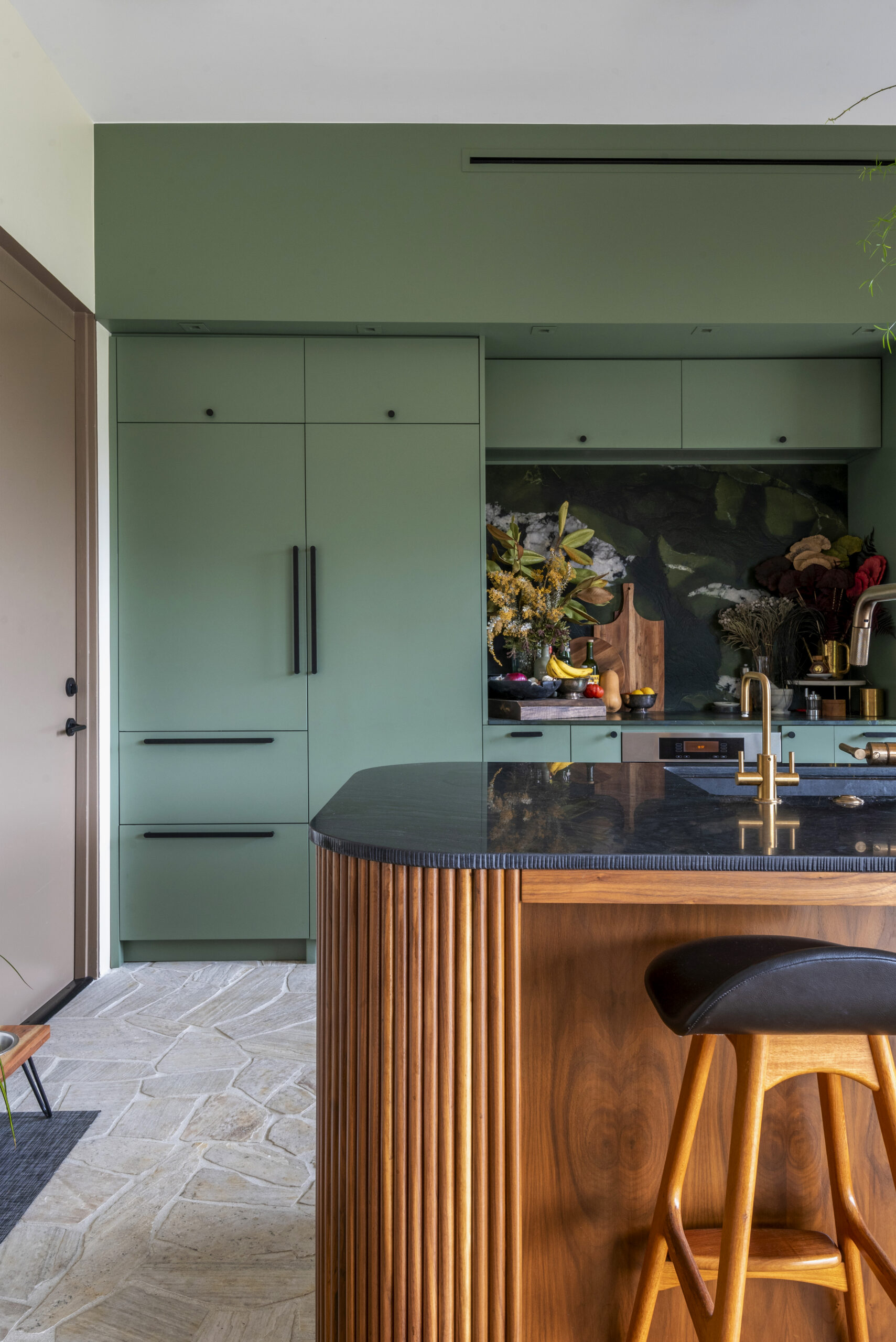 A remodeled kitchen in Los Angeles with dark green cabinets, wood-stained peninsula, and matte black cabinet hardware