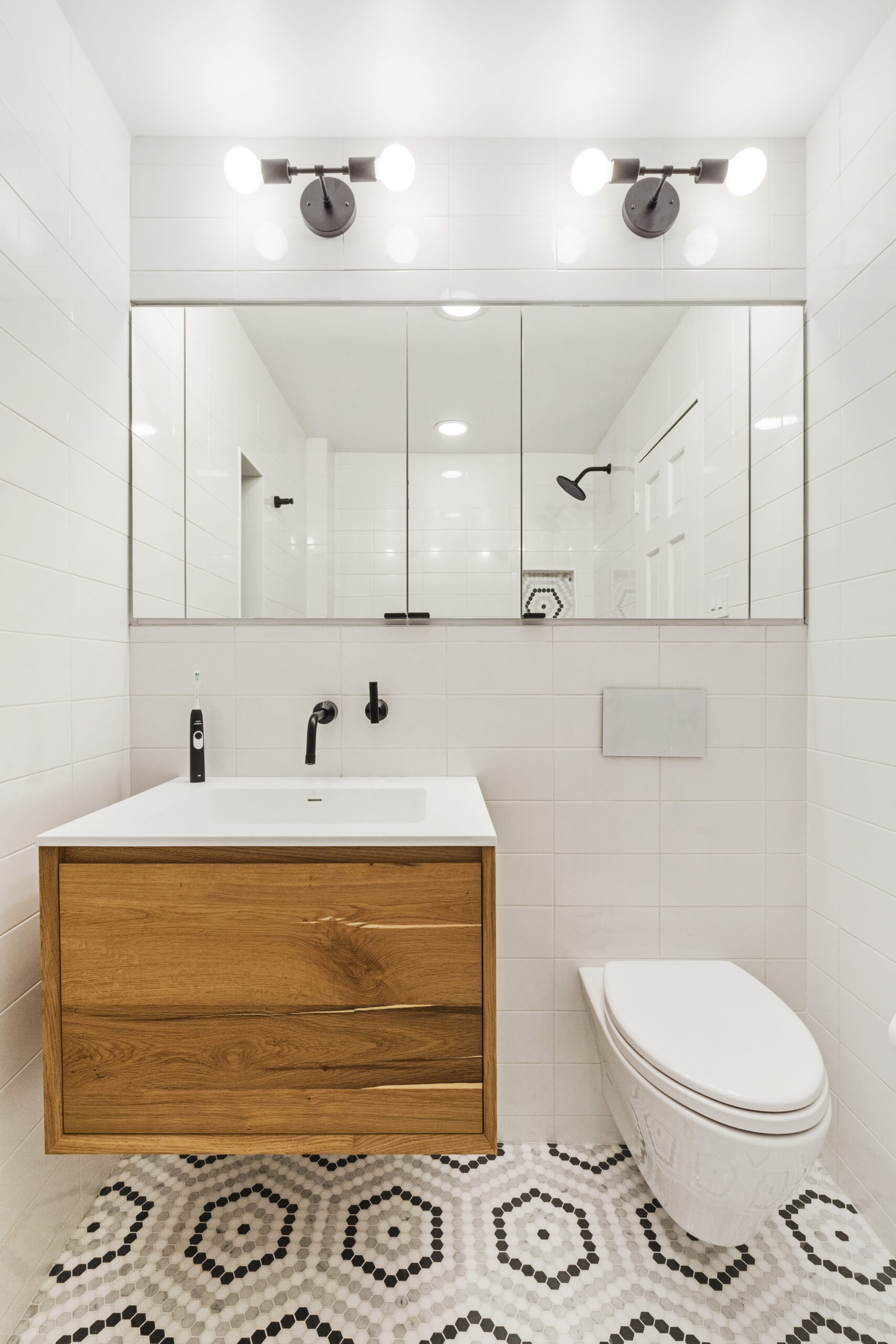 New bathroom features built-in rectangular mirror, overhead lighting, wood vanity and floating toilet