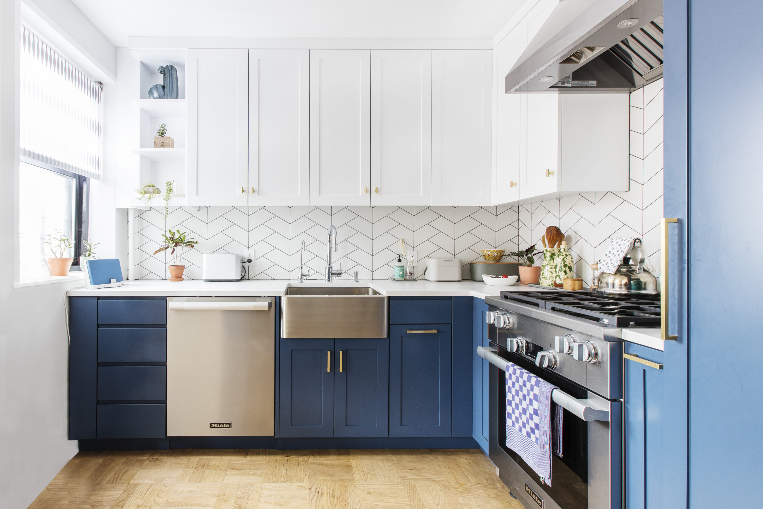A renovated kitchen with royal blue and white Shaker cabinets, warm brass pulls and knobs, and graphic backsplash