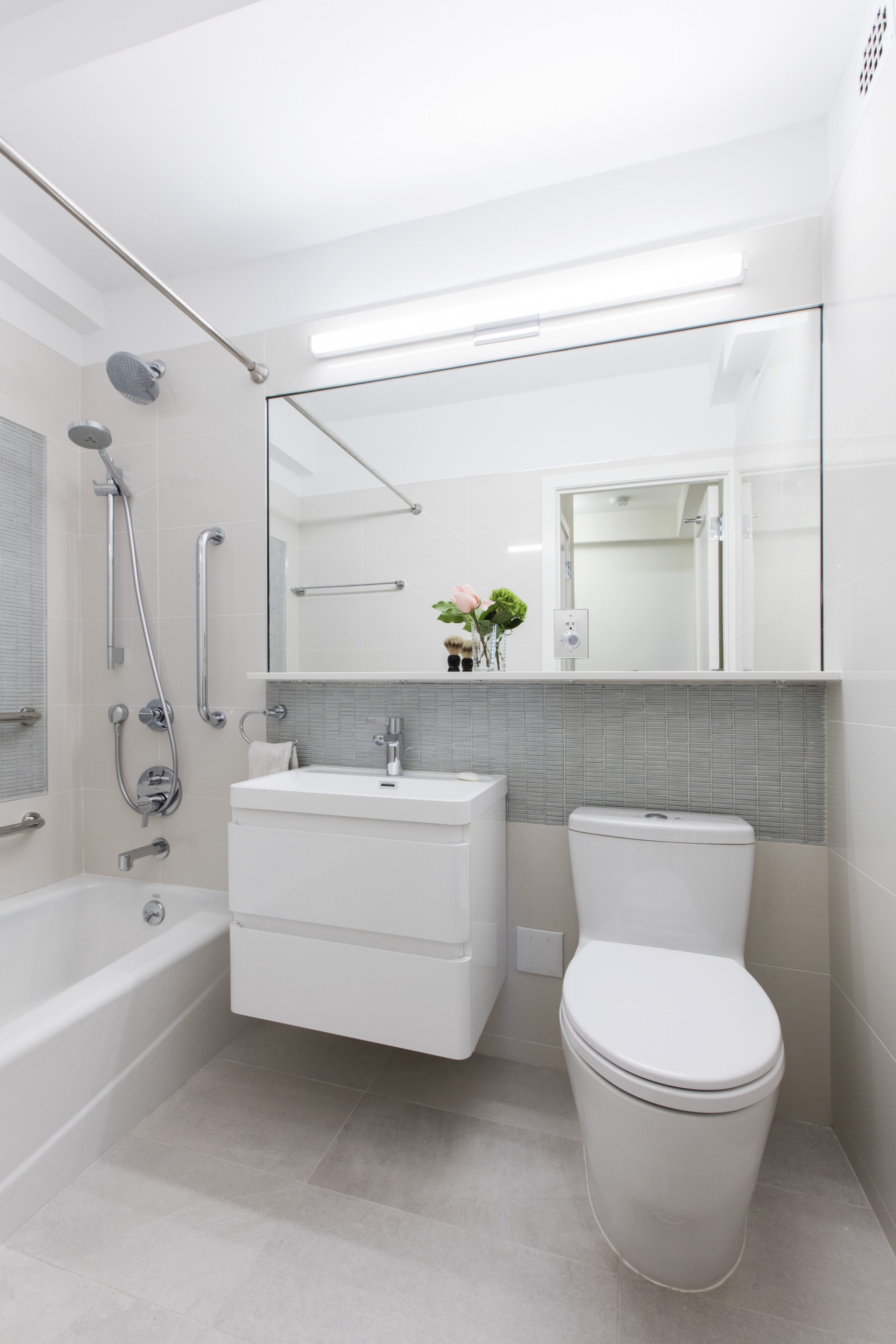 Remodeled bathroom with rectangular mirror, white floating vanity, toilet and bathtub with shower
