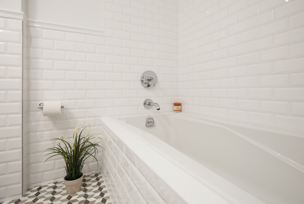 White bathtub, subway wall tile, geometric tile floor, and plant after a Park Slope bathroom remodel