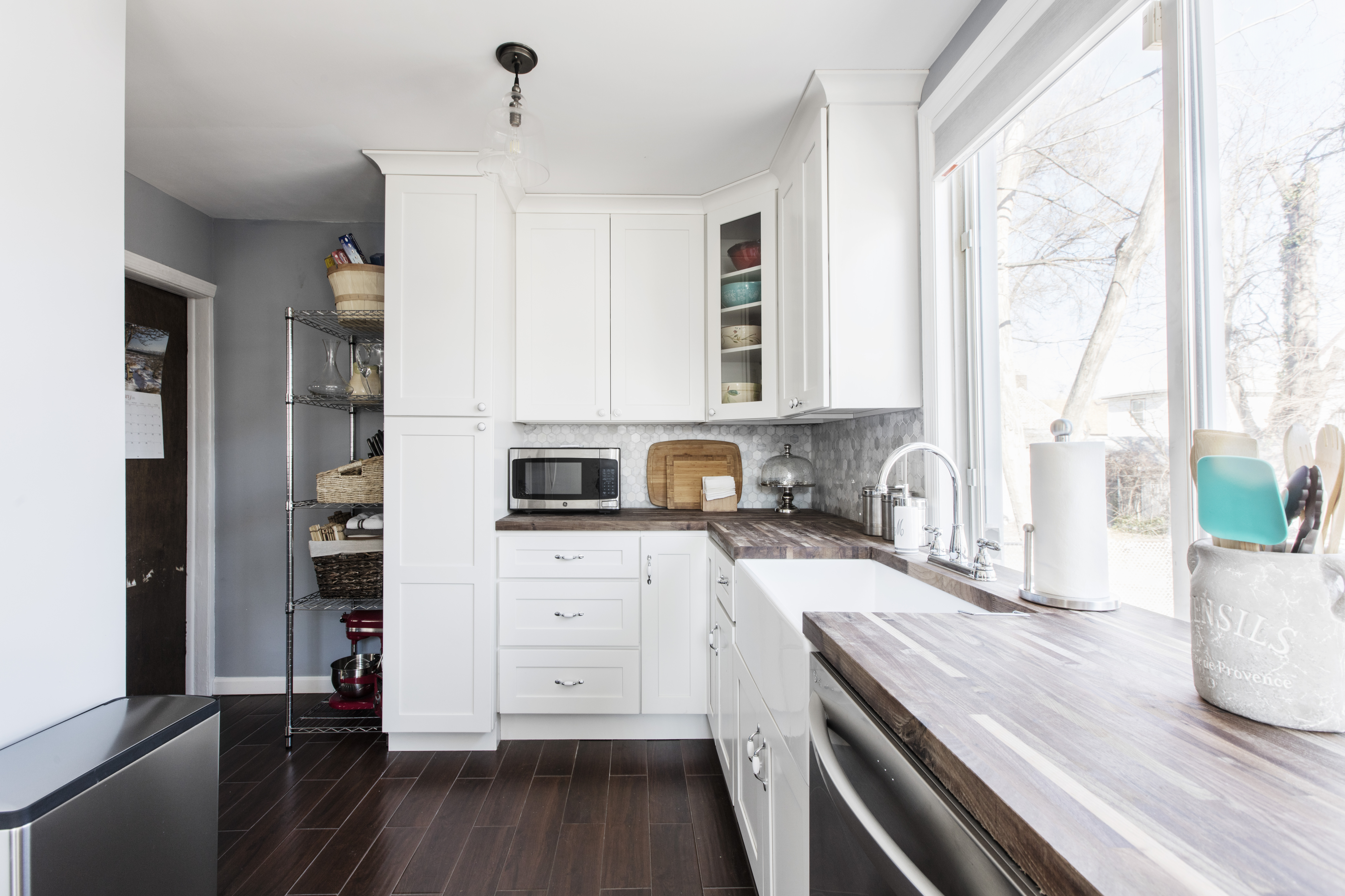 Historic home renovation kitchen in Jamaica with white ceiling-height cabinets, wood counters, gray tile, dark floors, and a sink under the window.