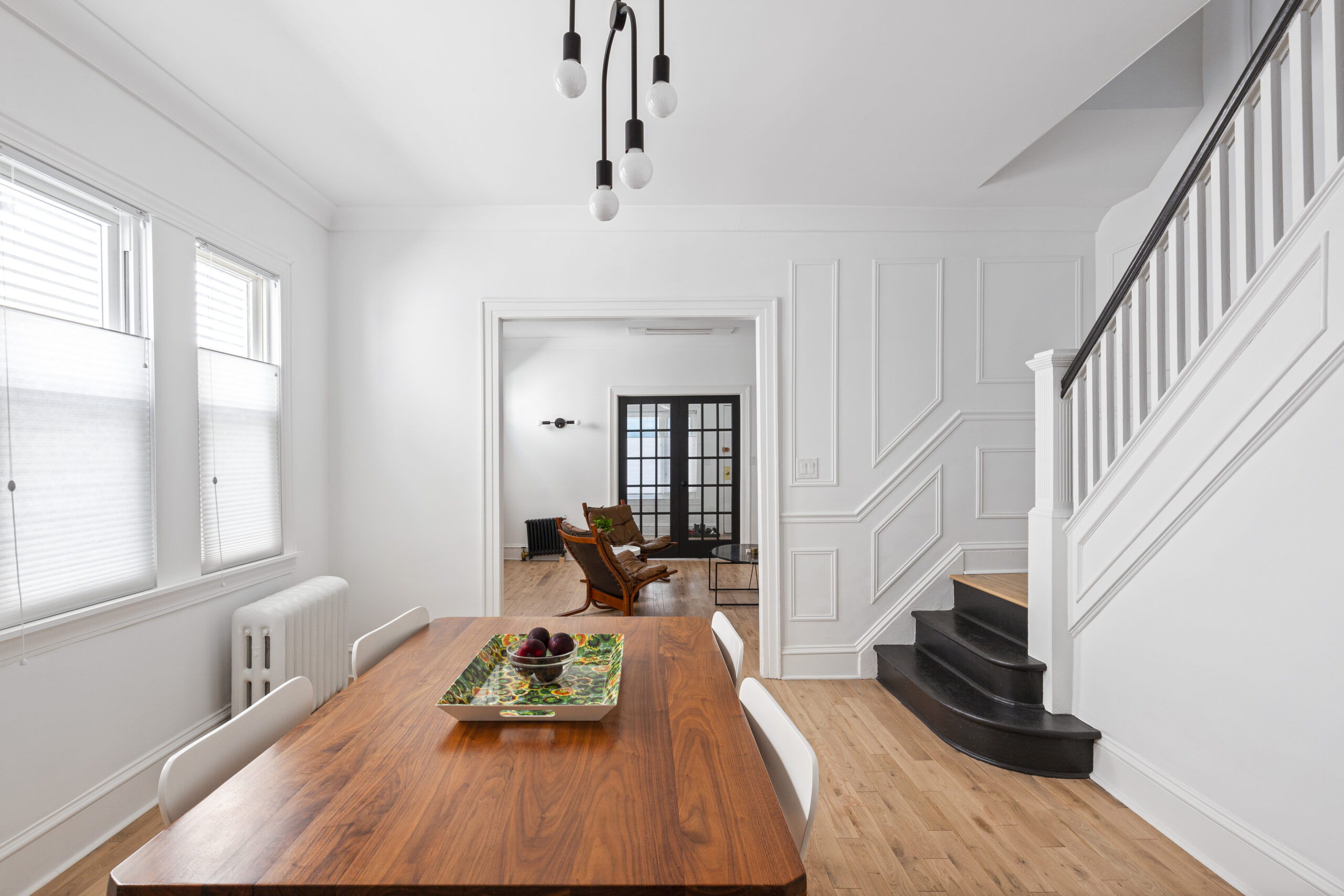 Midwood dining room after historic home renovation with restored wood floors, white trim, paneled stair wall, black steps, and bright windows.