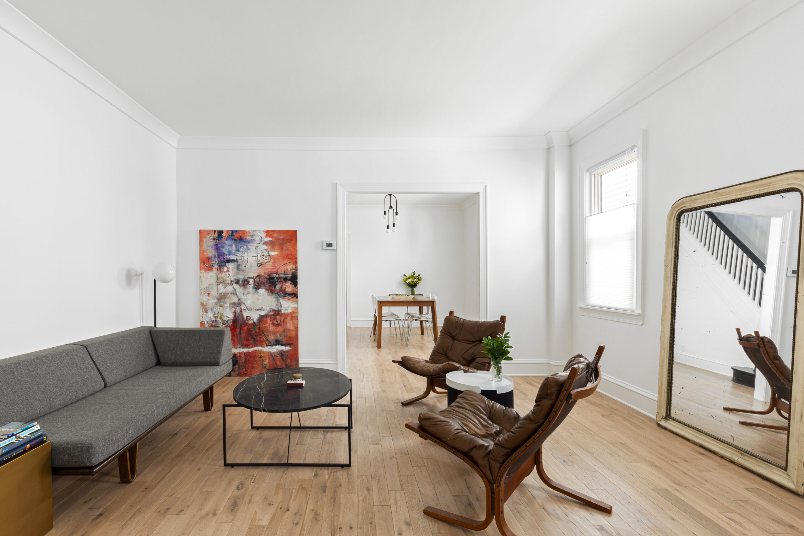 Midwood historic home renovation living room with restored wood floors, white walls, wide doorway to dining room, original trim, and mirrored stair view.