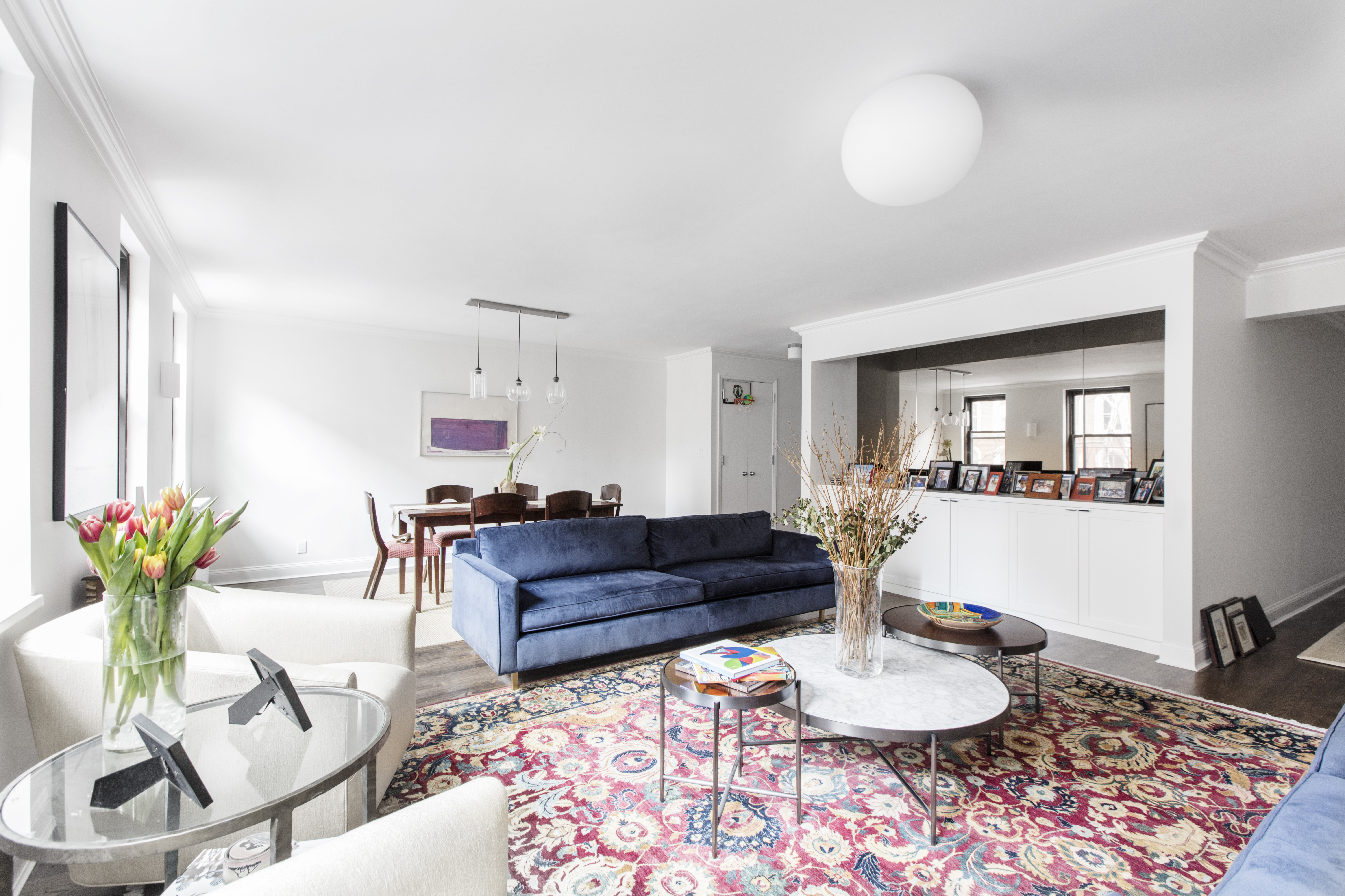 Upper East Side apartment combination with open living and dining areas, white walls, dark wood floors, blue sofa, built-ins, and wide windows.
