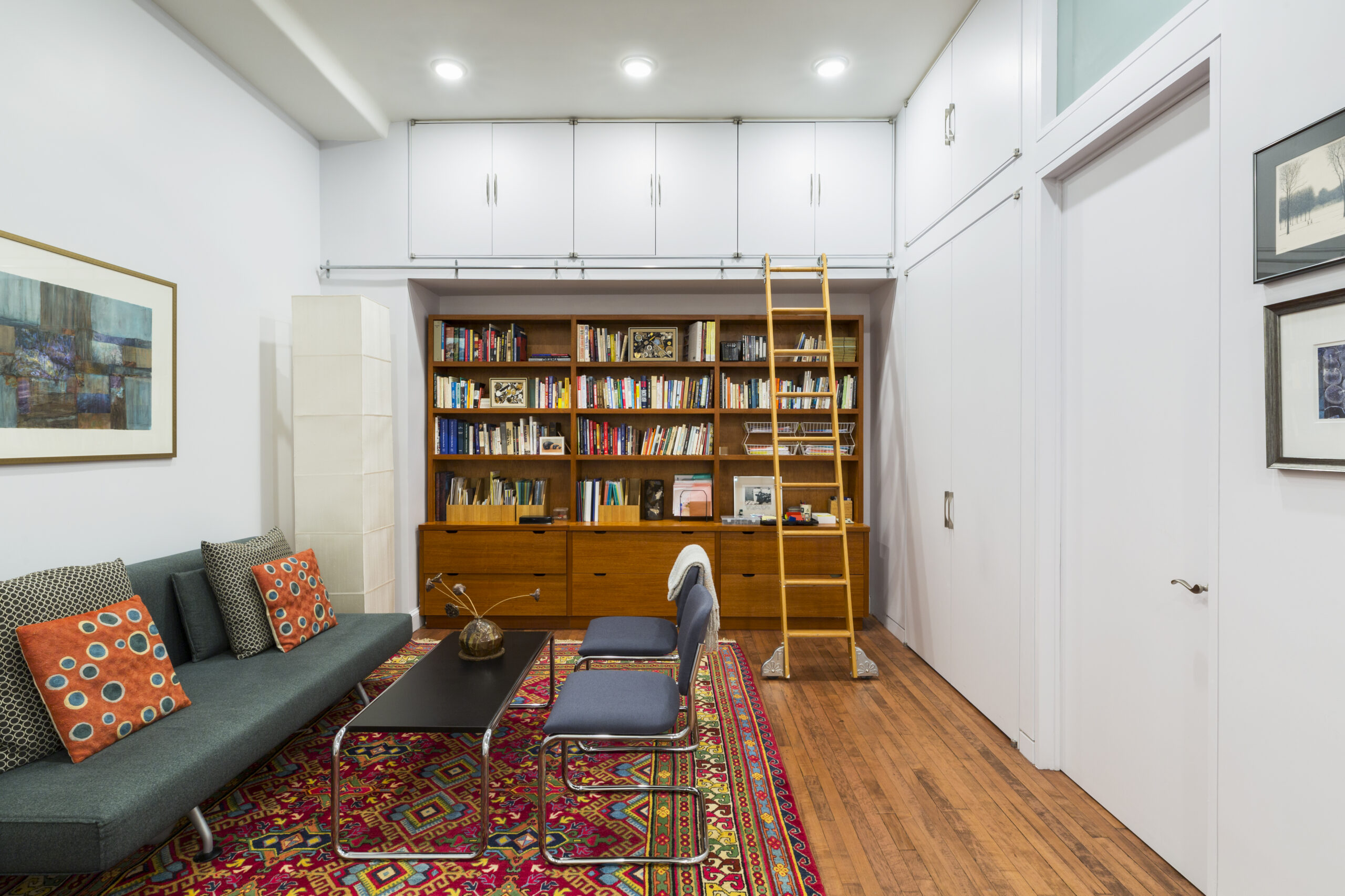 West Village whole-home remodel adds tall storage, library shelving, a rolling ladder, warm wood floors, and a cozy lounge area.