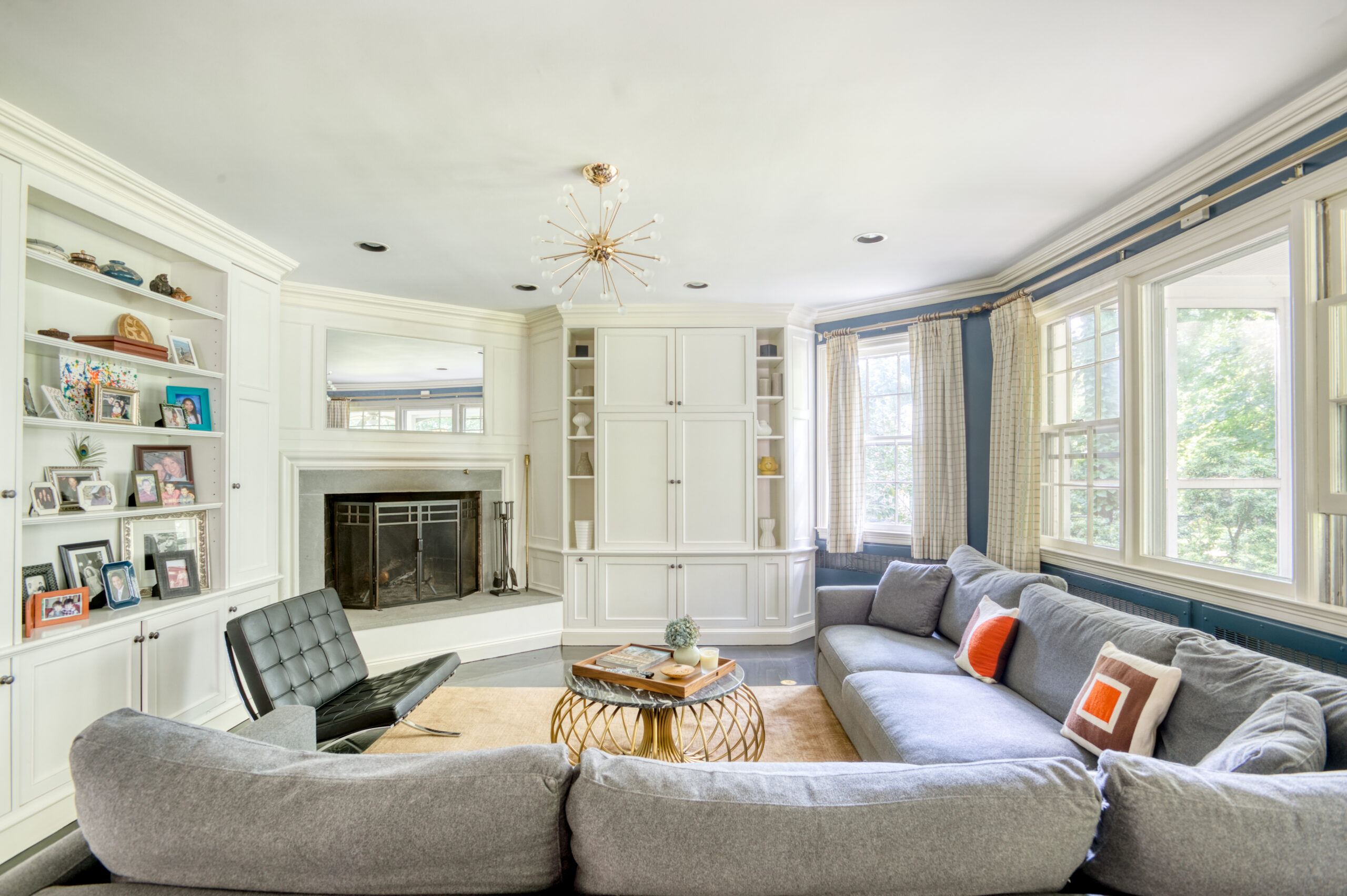 Westchester living room, part of a whole home renovation, with custom built-ins, a fireplace surround, blue walls, large windows, and a sputnik chandelier.