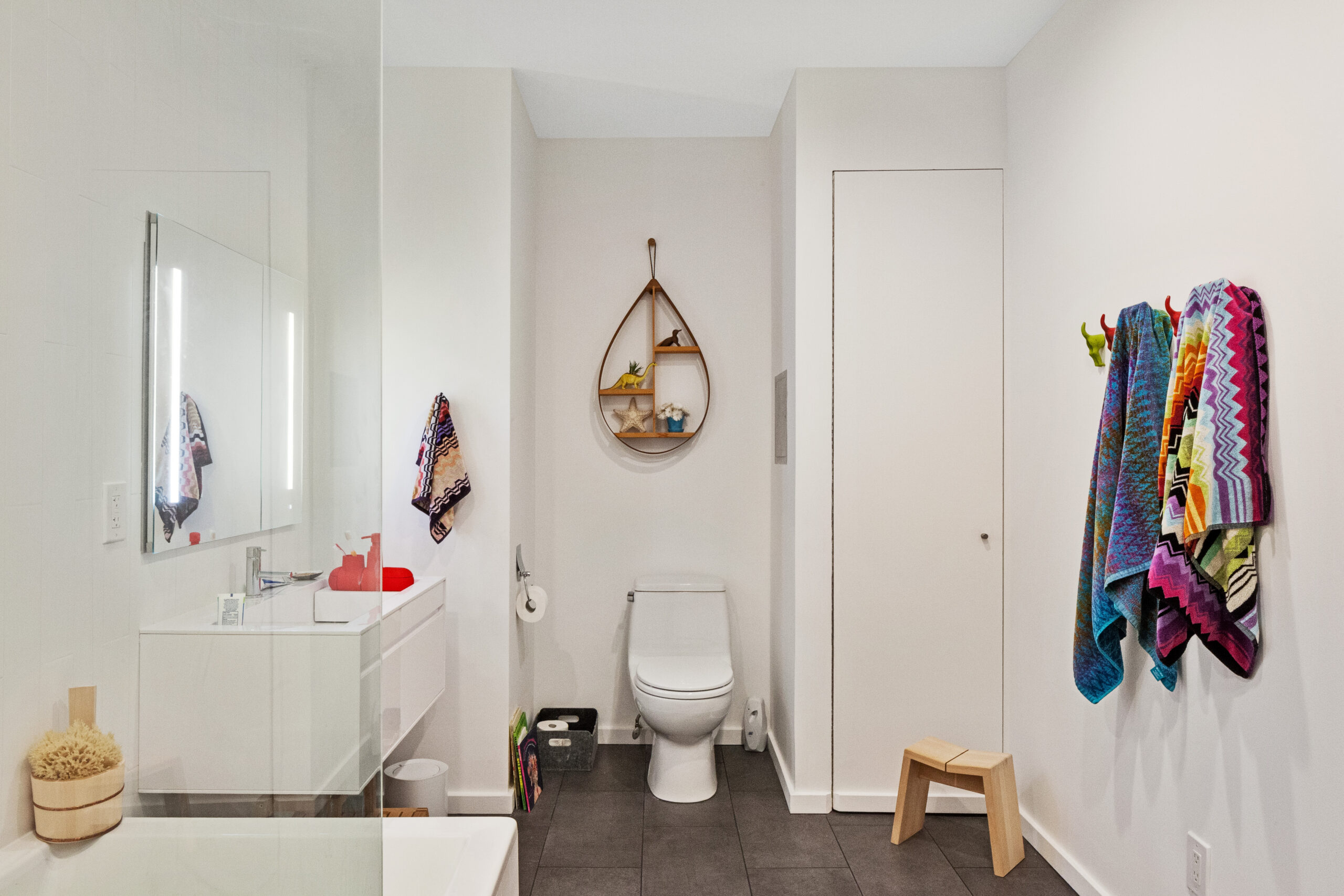 Gray slate tile grounds a remodeled Williamsburg bath with a glass partition, white vanity, recessed storage, and bright towels for a clean modern look.