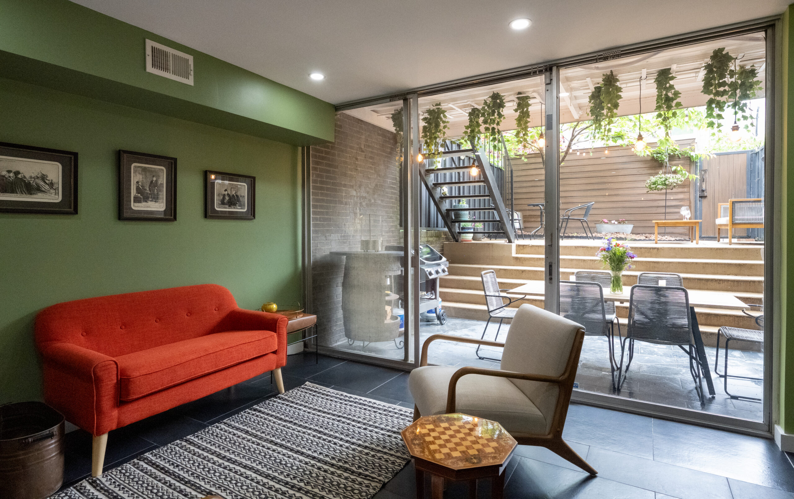 Washington, DC basement renovation with green lounge walls, orange sofa, black tile floors, glass patio doors, patterned rug, and outdoor seating.