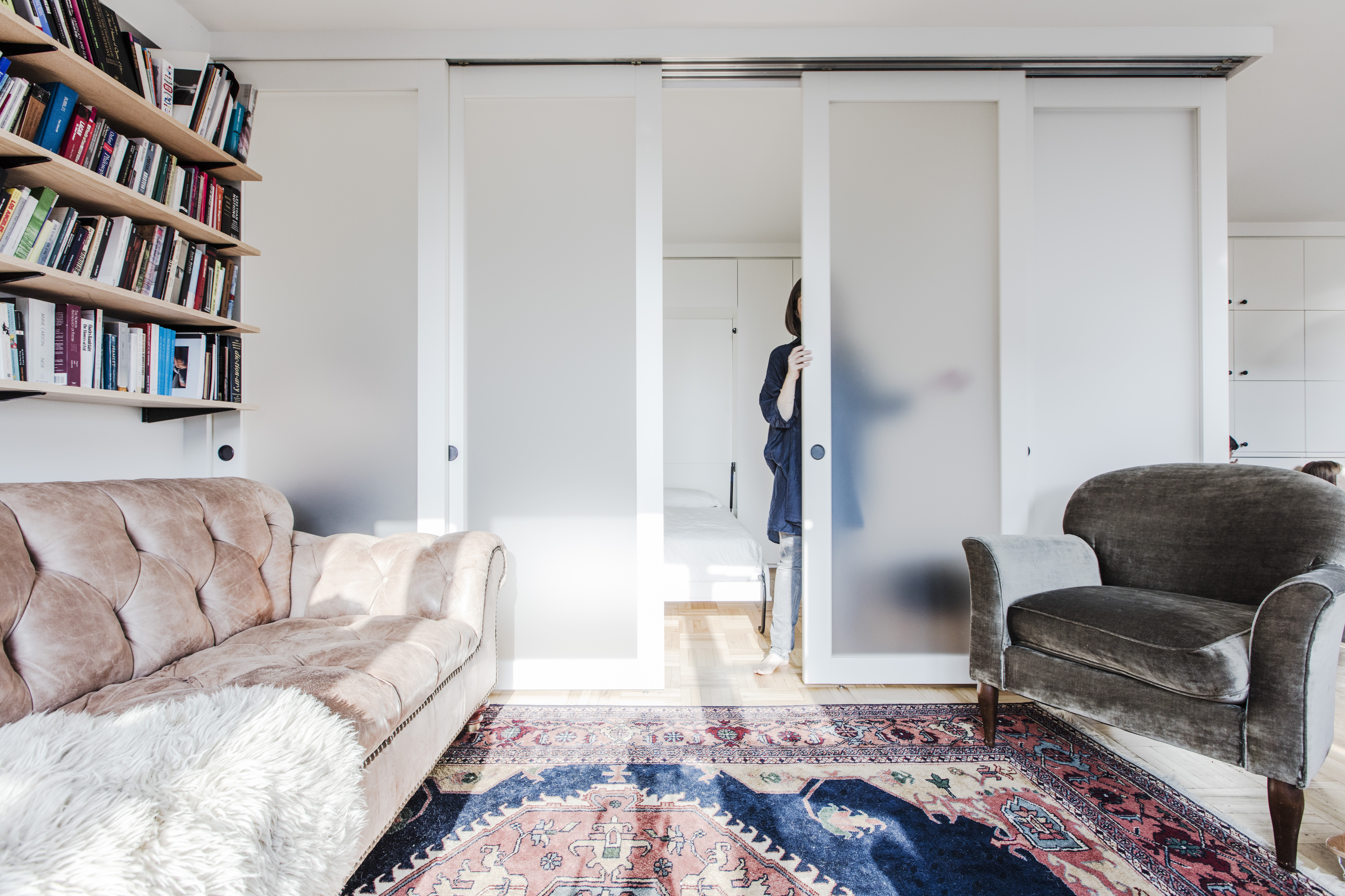 Frosted sliding room divider in Clinton Hill encloses a sleeping area while custom shelving and translucent panels preserve light in the living room.