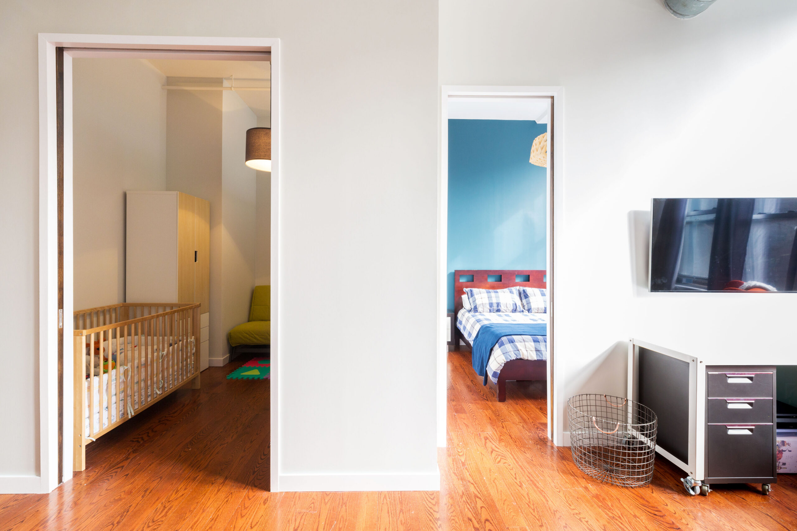 Full-height room divider walls in Downtown Brooklyn create two private bedrooms with open doorways and warm wood floors beside the living area.