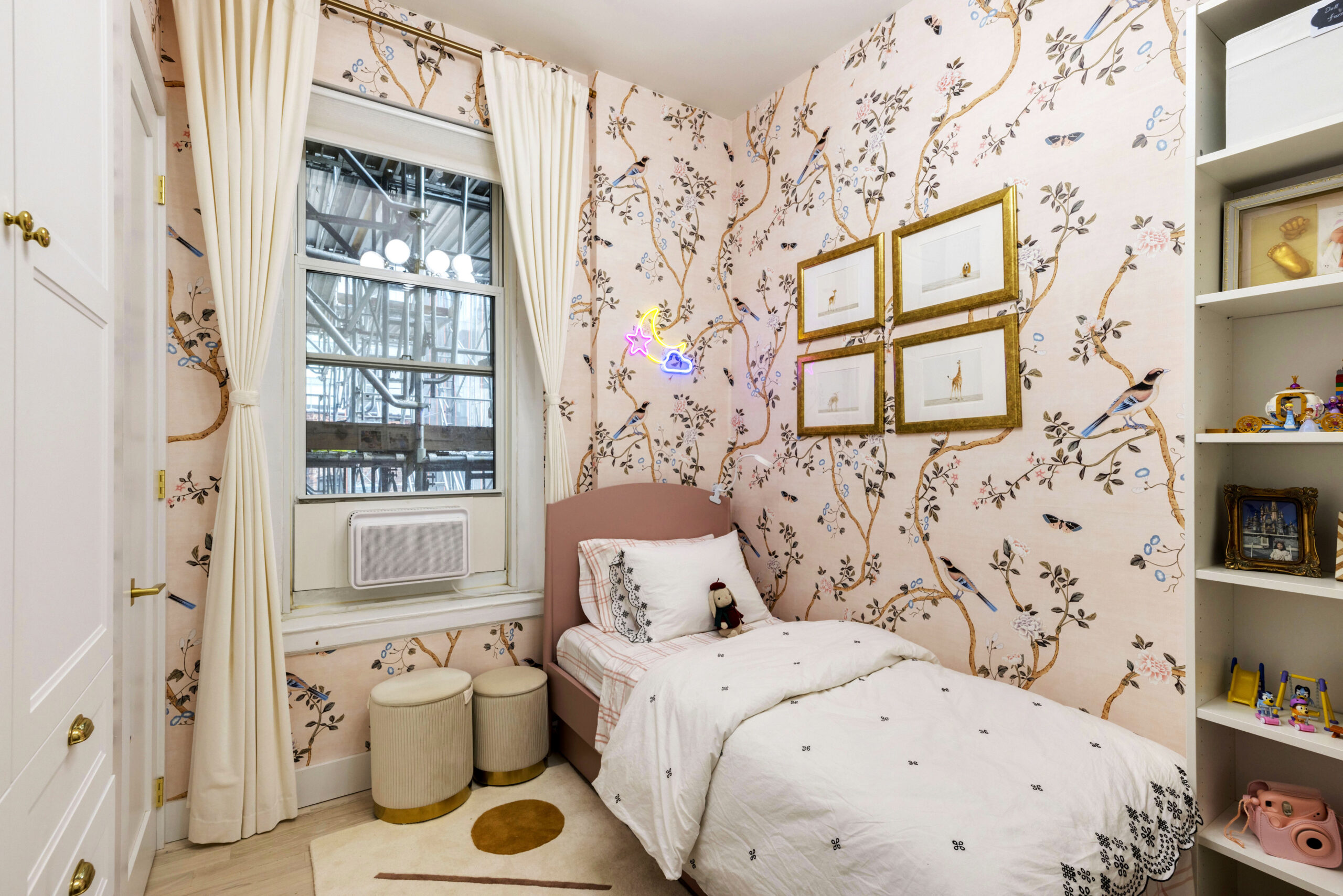 Upper East Side extra bedroom idea with pink bird wallpaper, twin bed, built-in shelves, tall curtains, and restored trim in a child’s room.