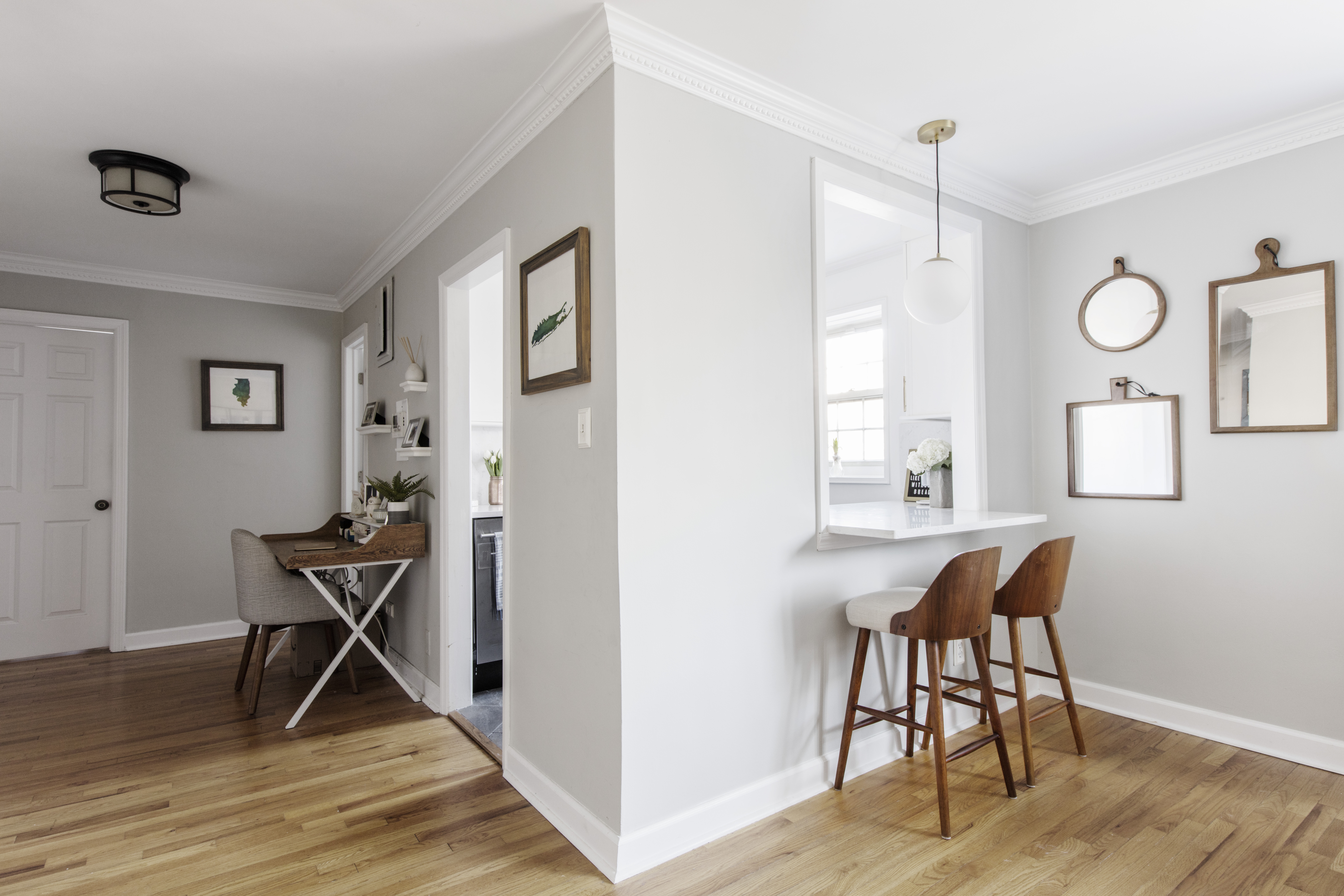 Forest Hills dining area with an enlarged kitchen pass-through, lowered white quartz counter, two wood stools, oak floors, and bright gray walls.