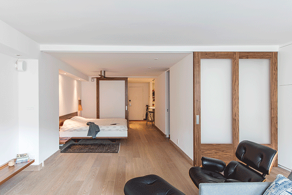 Folding walnut room divider panels in Gramercy Park open and close the sleeping zone, allowing the studio to shift between private and shared use.