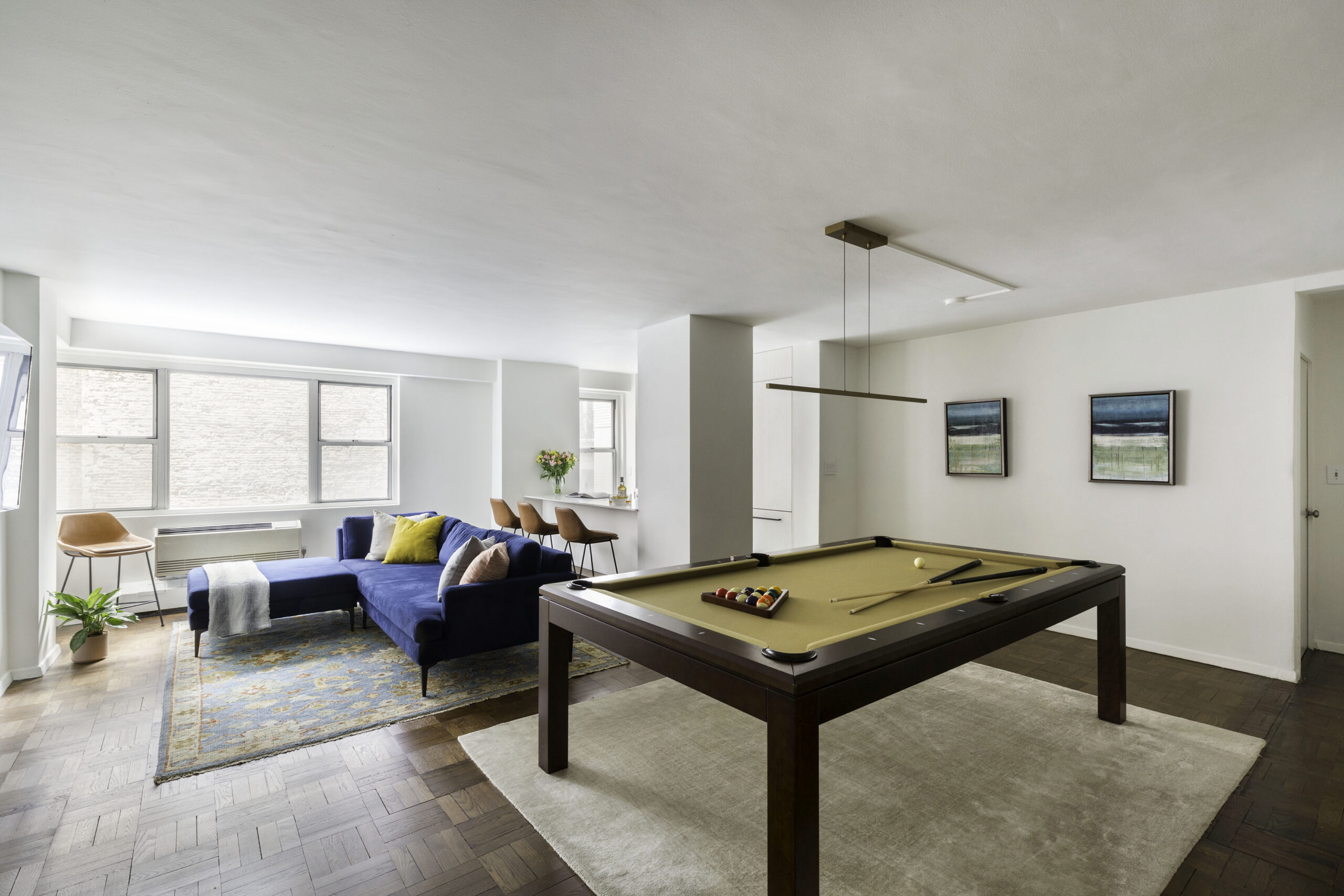 Greenwich Village living room with a pool table, wide kitchen opening, three-seat counter, blue sectional, parquet floors, and linear pendant lighting.