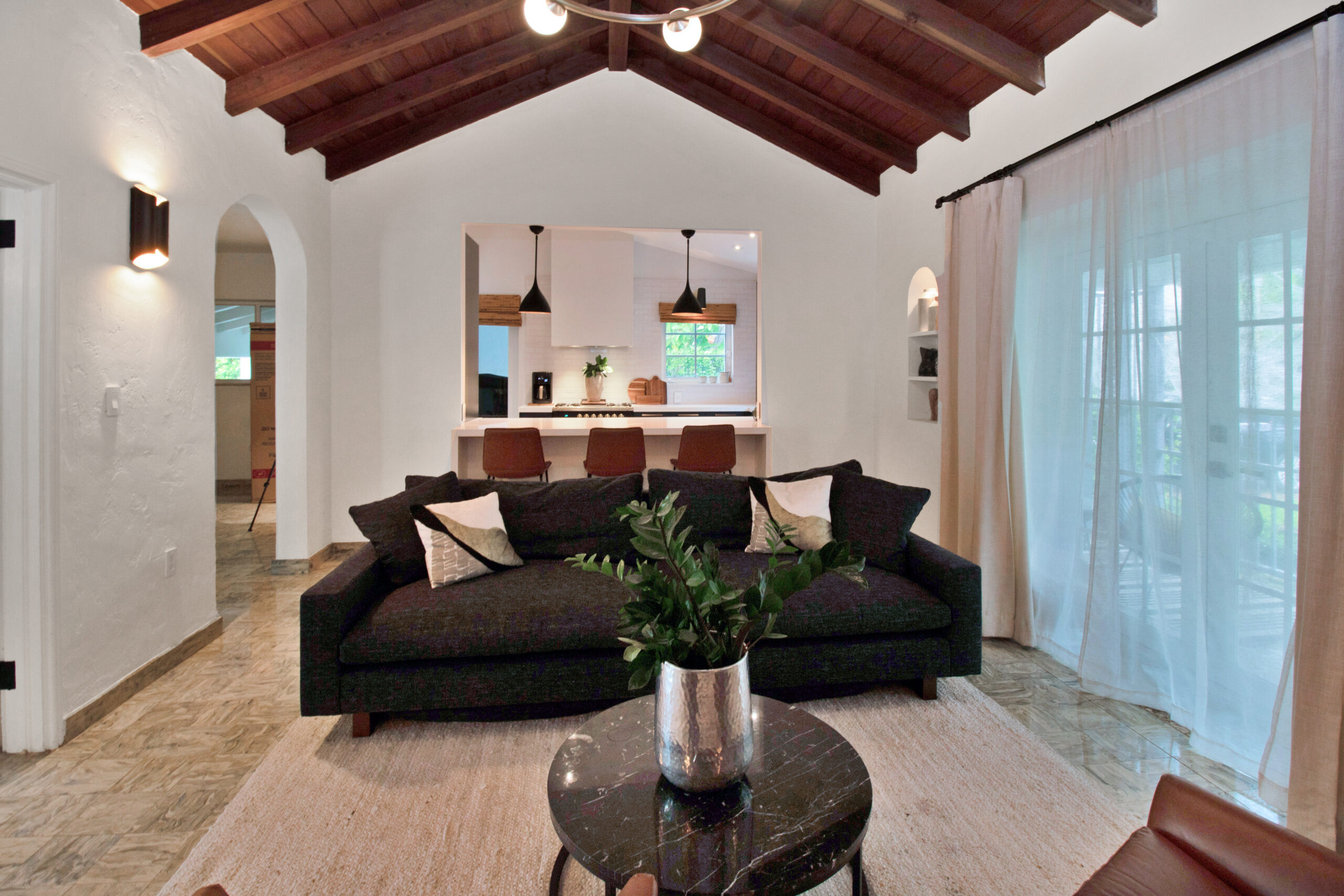 Miami living room with a wide kitchen pass-through, white quartz counter, three leather stools, dark cabinets, pendant lights, and tiled floors.