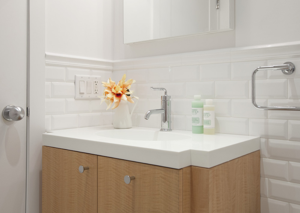 Park Slope bathroom with round chrome vanity knobs, a pale wood cabinet, white integrated sink, single-handle faucet, subway tile, and a towel bar.