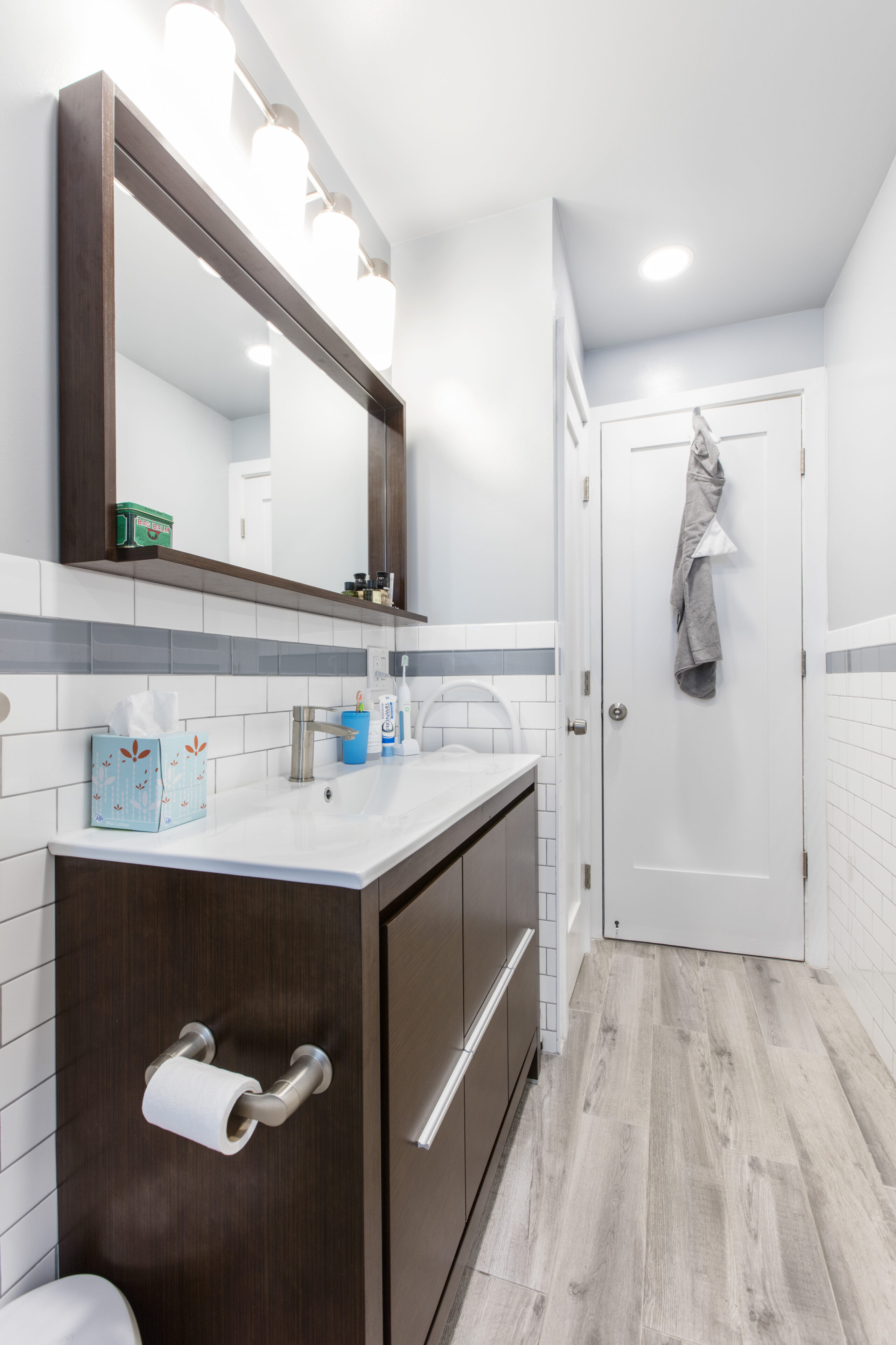 Sunset Park bathroom with a toilet paper holder mounted to the dark wood vanity, long brushed metal drawer pulls, a wide mirror, and a door hook.