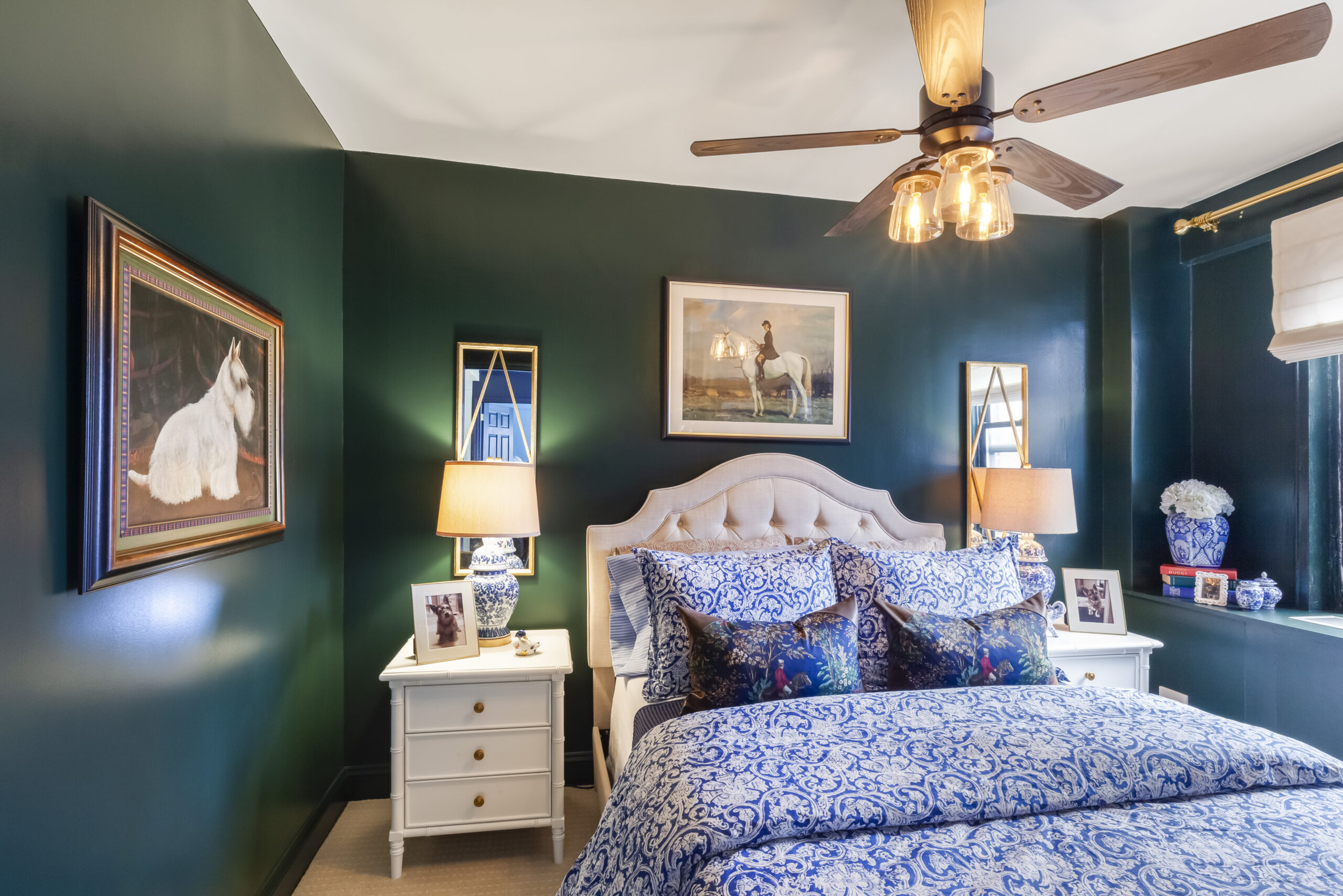 Sutton Place bedroom renovation with deep green walls, blue patterned bedding, white nightstands, framed art, brass accents, and ceiling fan.