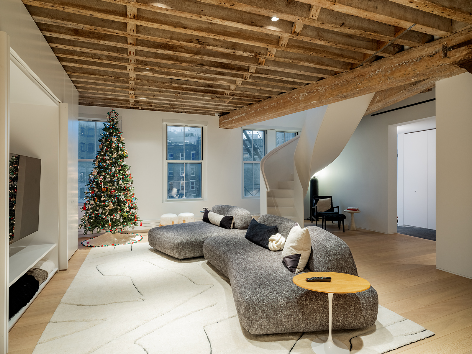 A Tribeca staircase renovation idea pairs a sculptural white stair with exposed timber beams, pale oak floors, and an open-plan living room.
