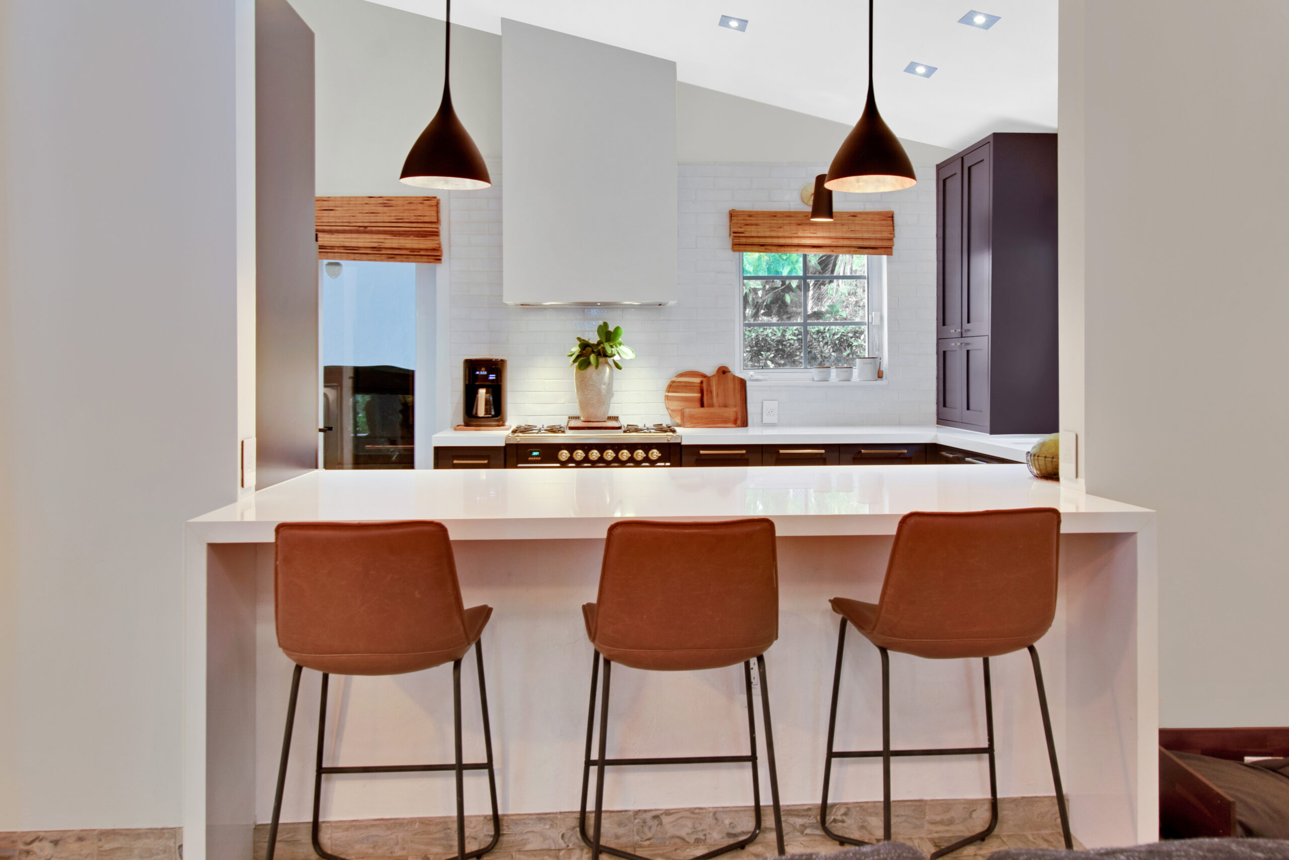 Upper Eastside kitchen pass-through with an eight-foot white counter, three leather stools, dark Shaker cabinets, pendant lights, and tile backsplash.
