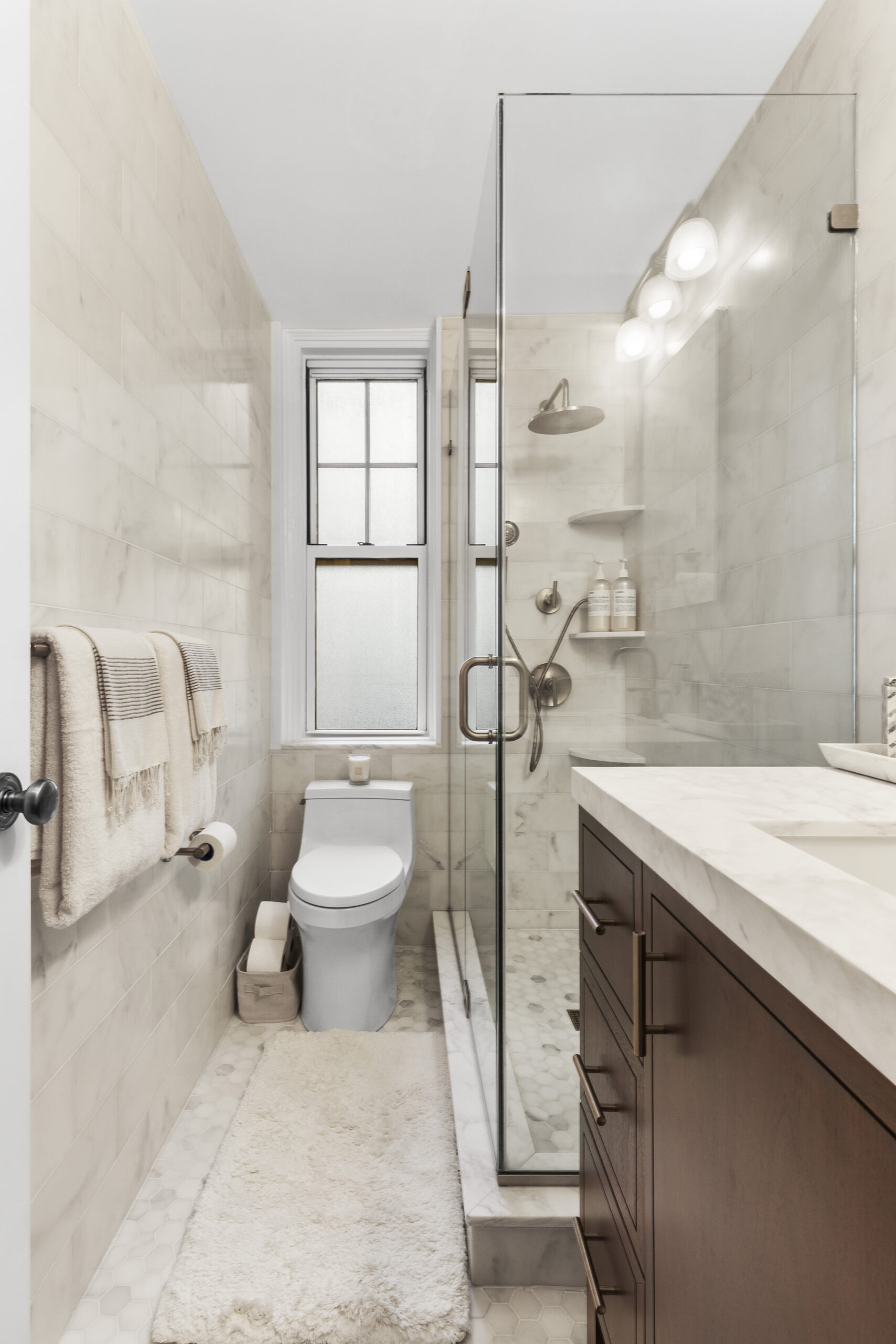 West Village bathroom with matching vanity pulls, shower fixtures, towel bars, and glass enclosure hardware set against Calacatta tile.