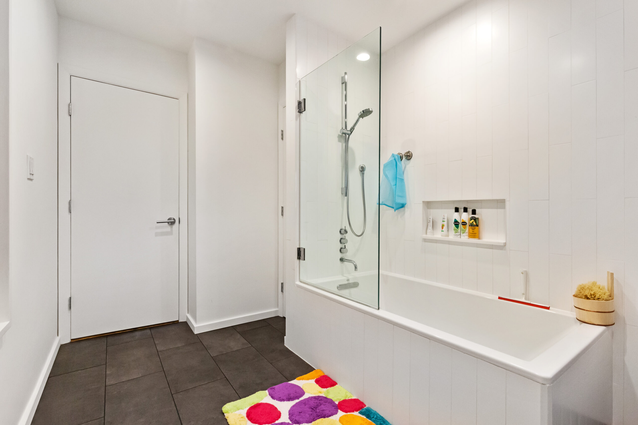 Williamsburg bathroom with a fixed glass tub panel, white vertical wall tile, dark slate flooring, a recessed niche, and chrome shower hardware.