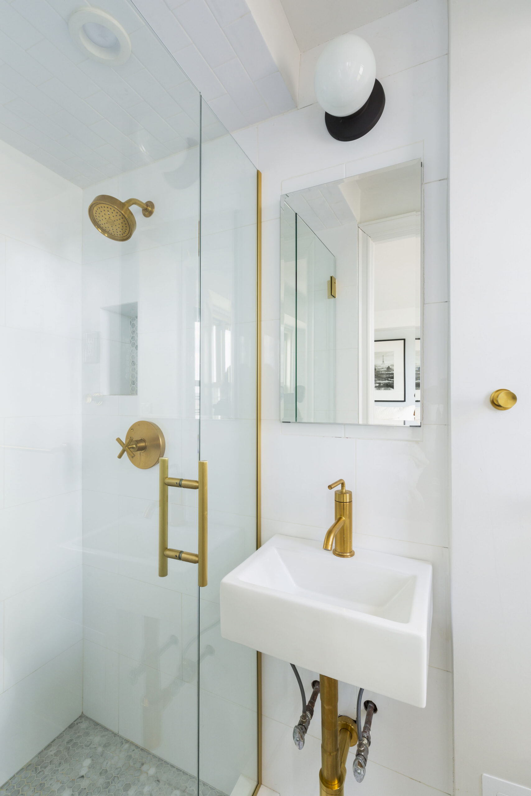 Small bathroom with brass fixtures, overhead lighting, and white shower tile
