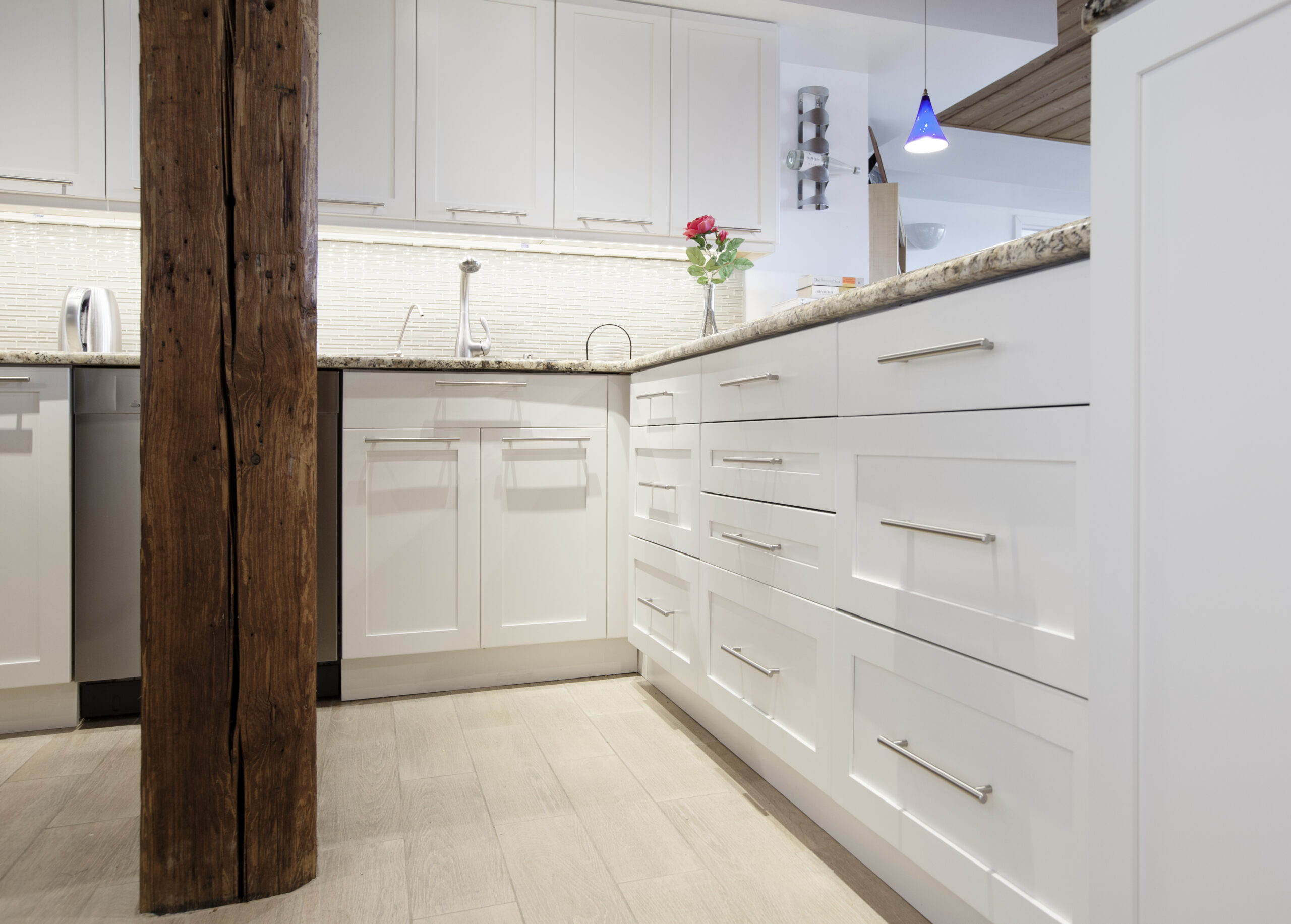 Brooklyn kitchen with white corner cabinetry, deep drawers, granite counters, stainless hardware, and exposed wood columns framing the layout.
