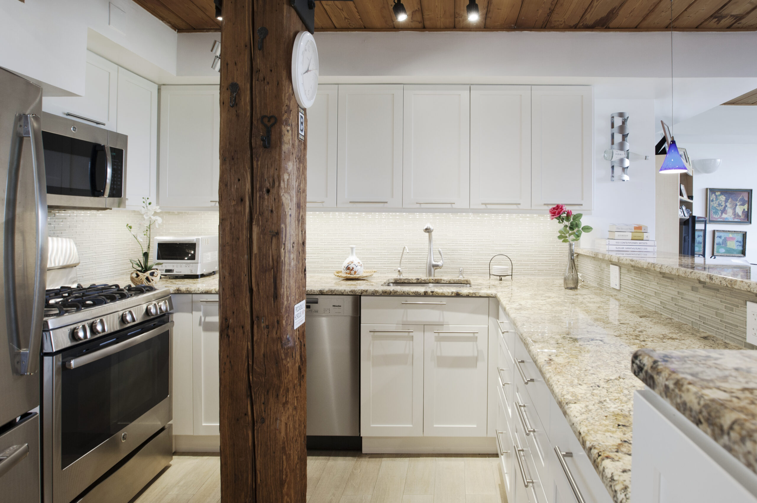 Carroll Gardens kitchen with white corner cabinets, granite counters, stainless appliances, mosaic backsplash, and exposed wood beams.