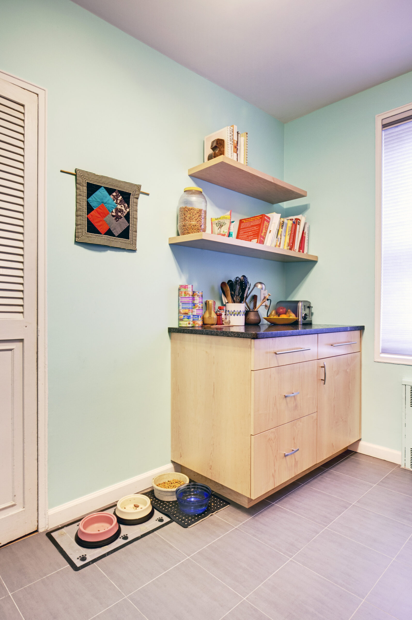 Windsor Terrace corner built-in with maple cabinetry, dark countertop, open wood shelves, deep drawers, pantry storage, and gray tile flooring.