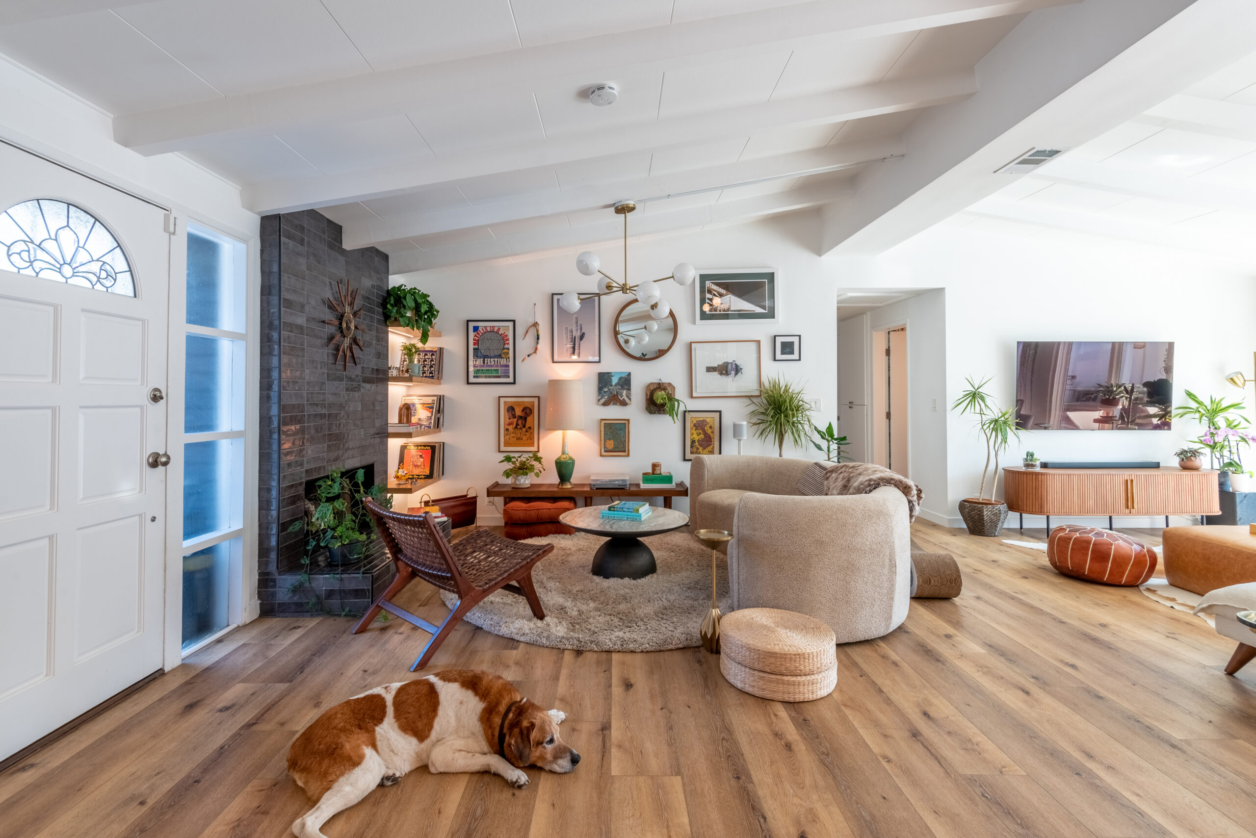 Culver City living room with dark elongated fireplace tile, white beamed ceiling, wood floors, curved seating, media console, and open-plan layout.