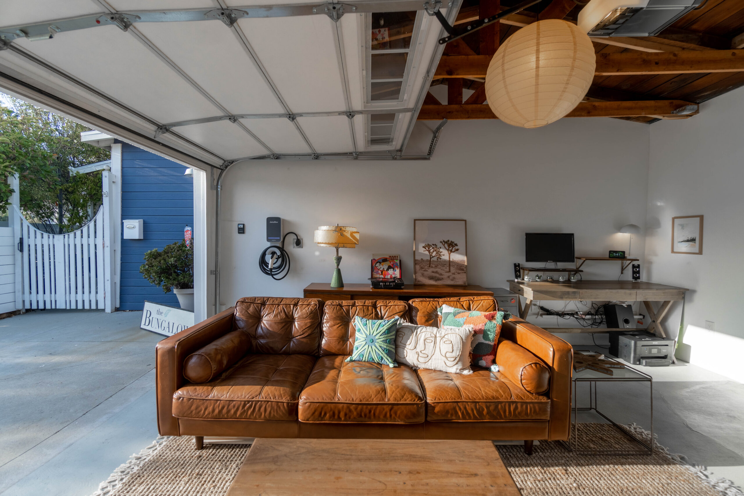 Inglewood garage remodel with exposed rafters, an operable overhead door, leather seating, a work desk, and an electric vehicle charger.