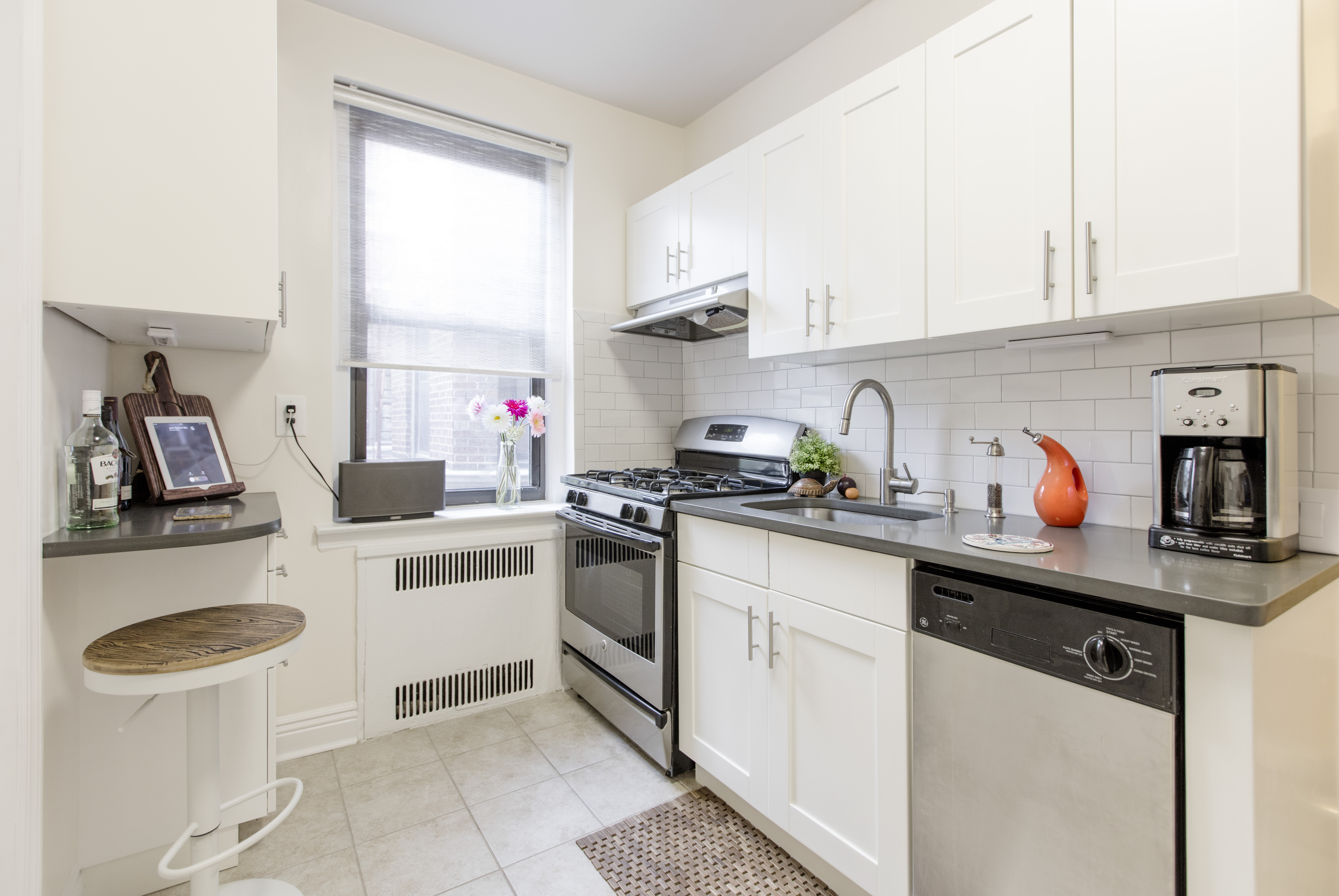 Prospect Park South kitchen with white corner cabinets, gray counters, subway tile backsplash, stainless appliances, and a compact breakfast ledge.