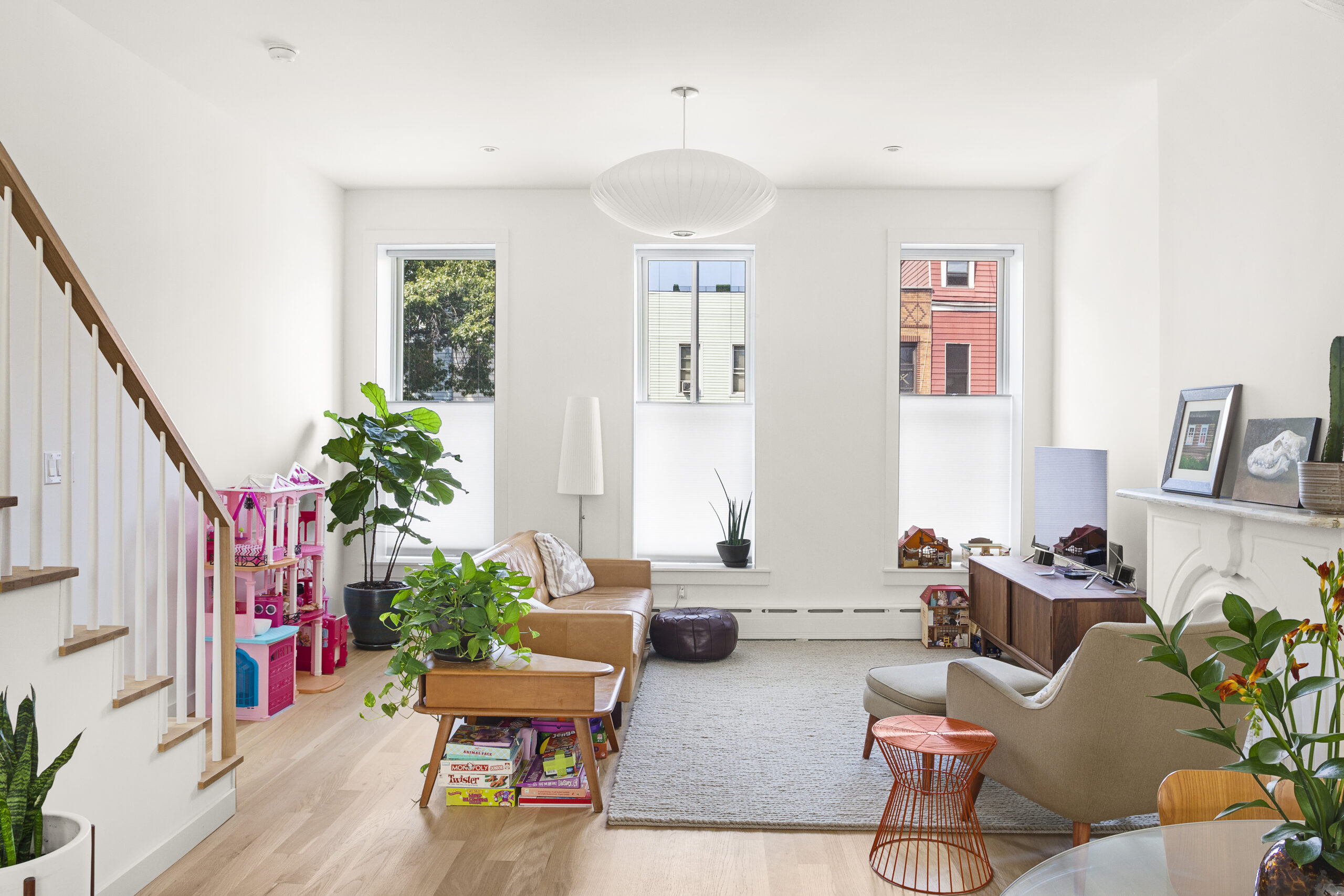 Bedford-Stuyvesant townhouse living room with white oak floors, rebuilt white-and-wood stairs, tall windows, mid-century seating, and an open layout.