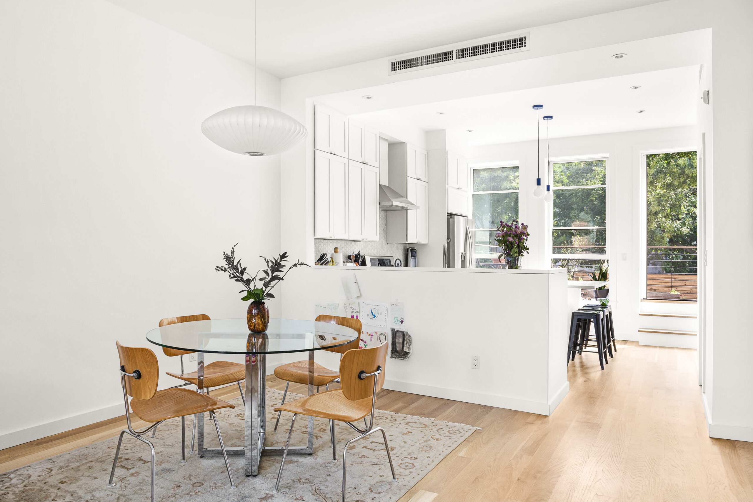 Bedford-Stuyvesant townhouse layout with open dining and kitchen areas, white oak floors, a glass table, pendant lighting, and views toward the rear.