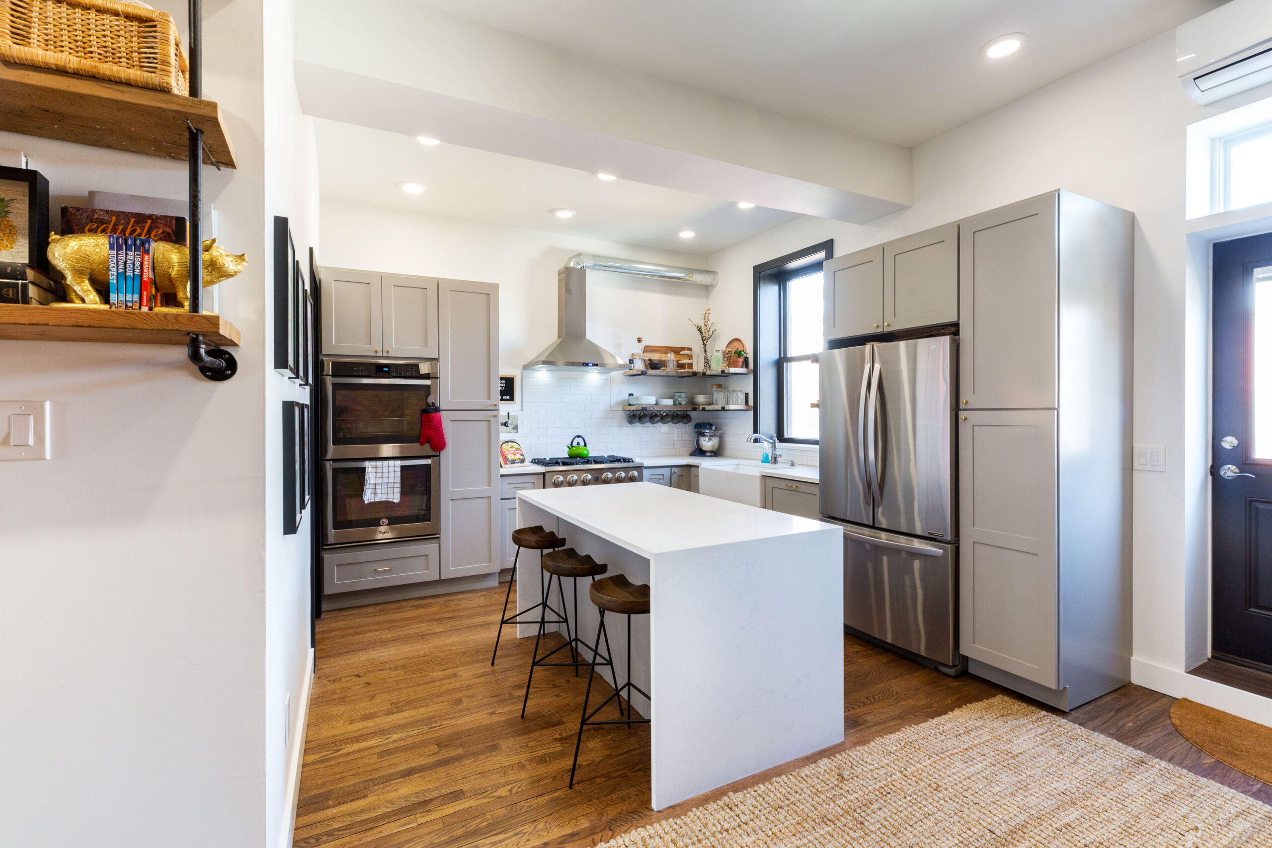 Brooklyn townhouse remodel with gray cabinetry, white island seating, wood floors, stainless appliances, open shelving, and a bright garden-level rental kitchen.