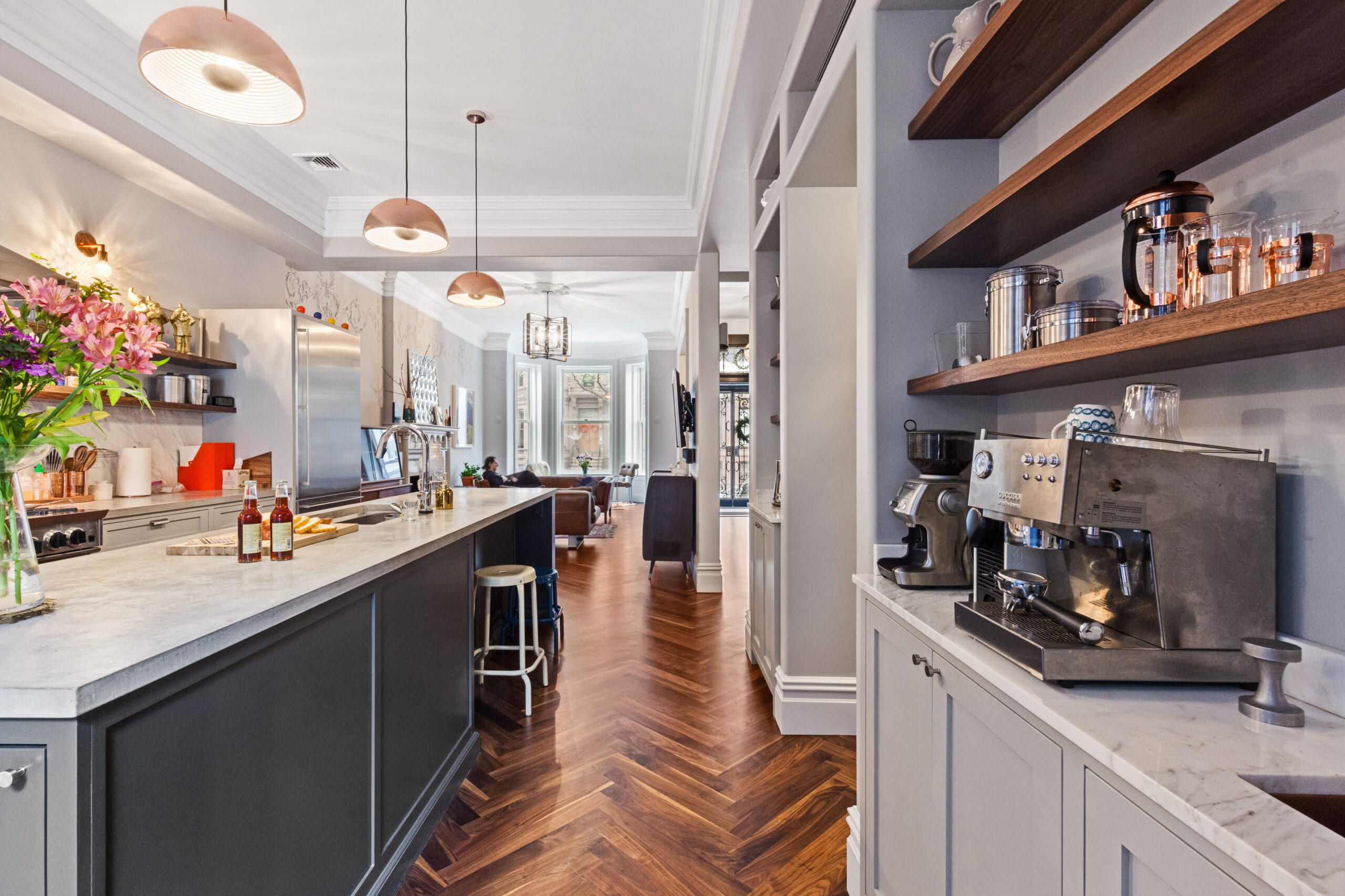 Herringbone walnut flooring, a marble-topped island, open shelving, pendant lights, and a built-in coffee bar in this renovated Brooklyn kitchen.