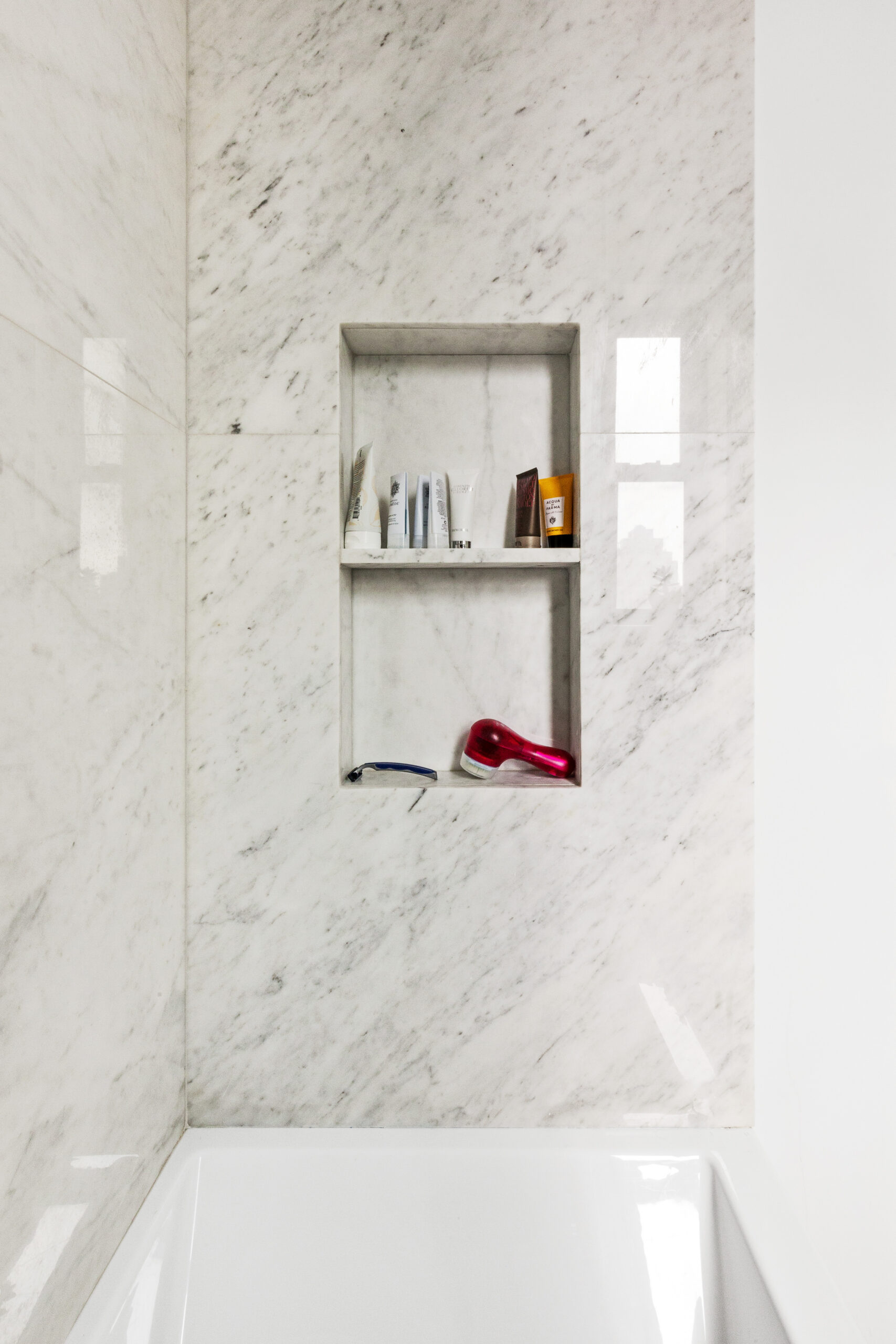 A tall two-tier shower niche blends into veined marble walls, creating recessed storage with a seamless built-in appearance in this Chelsea bathroom.
