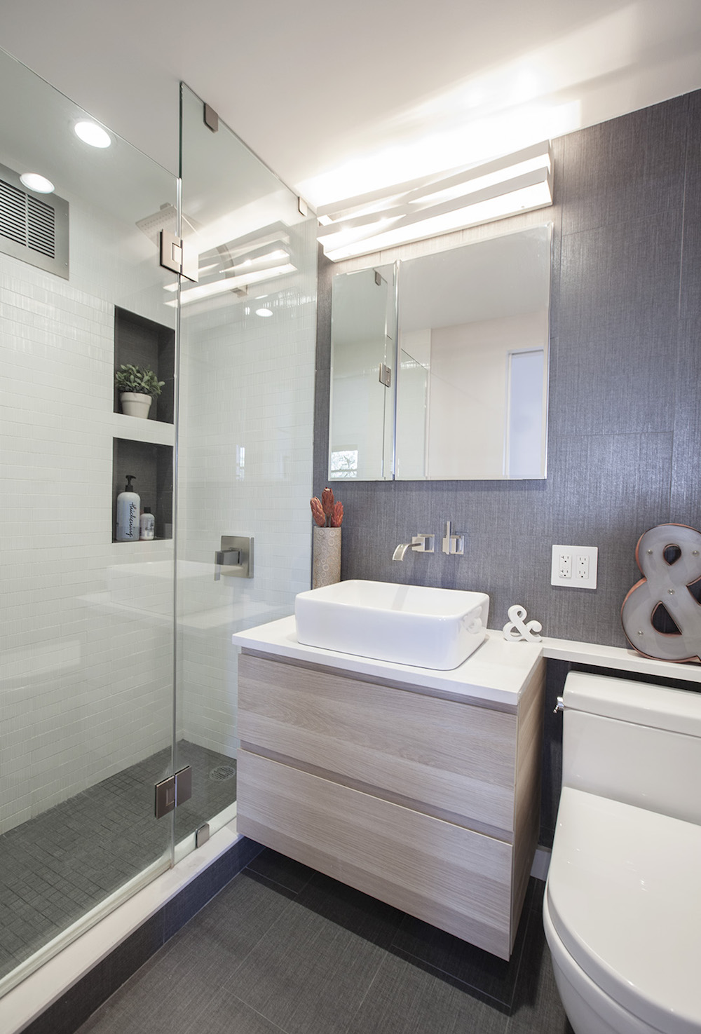 Two stacked shower niches with dark interiors contrast against glossy white tile beside a glass shower enclosure in this Clinton Hill bathroom.