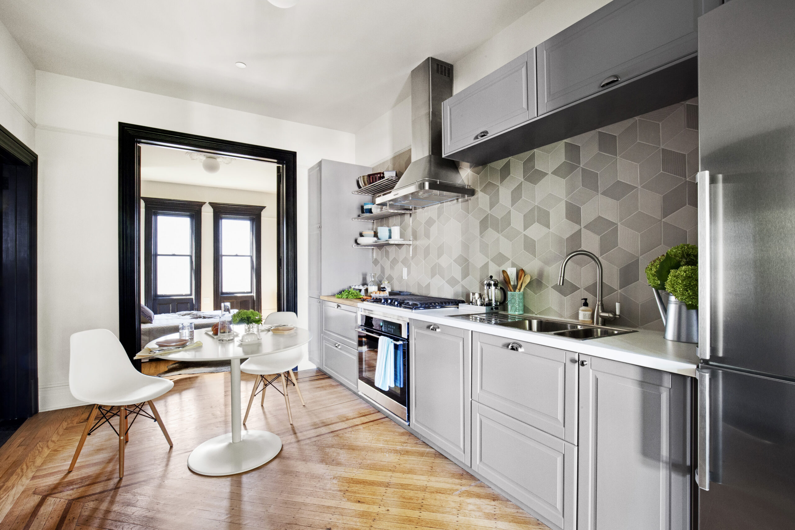 Crown Heights townhouse kitchen with gray cabinetry, geometric backsplash tile, restored wood floors, dark trim, and an open connection to dining space.
