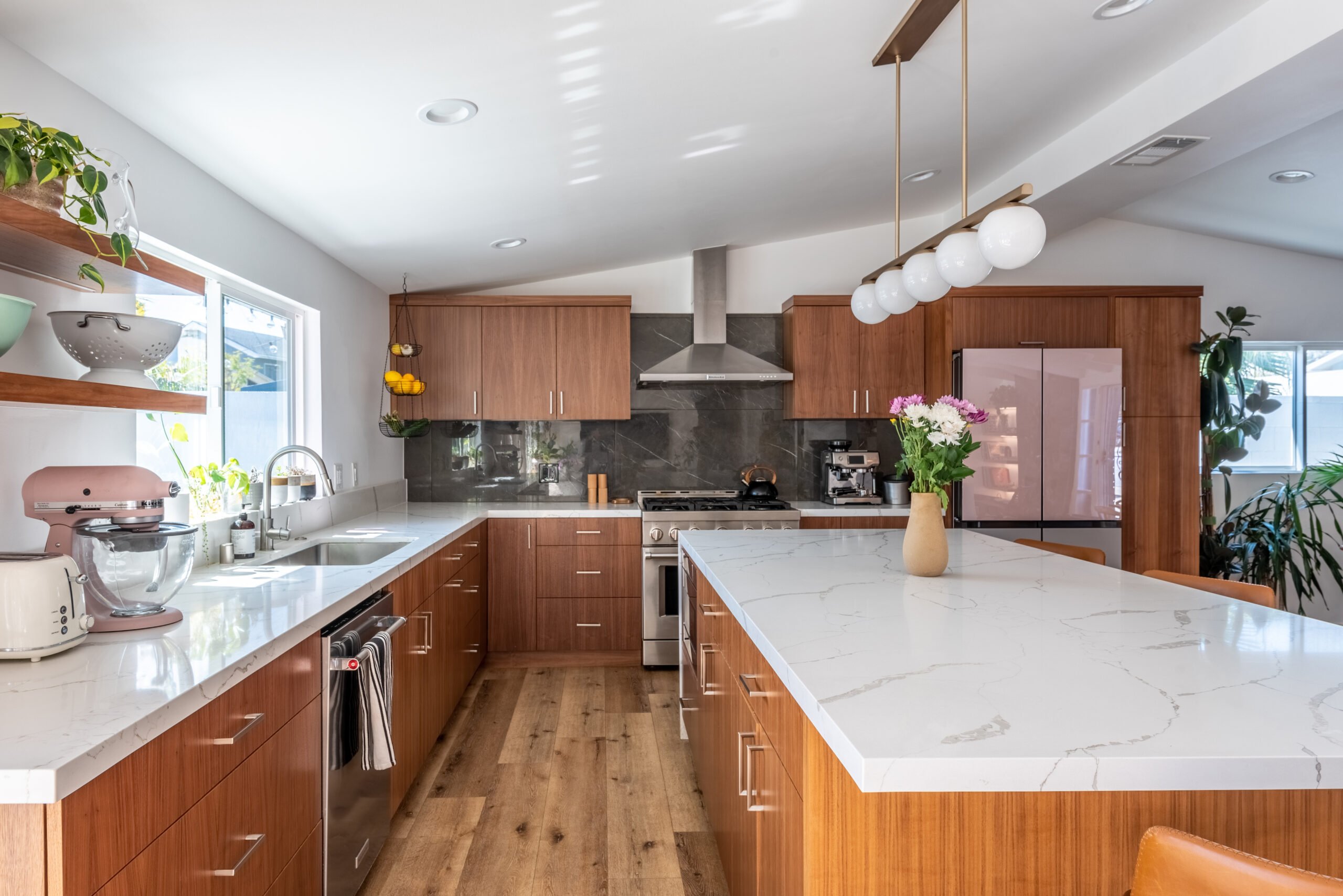 An open Culver City kitchen with walnut cabinets, a spacious white island, globe pendant lighting, and an unobstructed connection to dining.