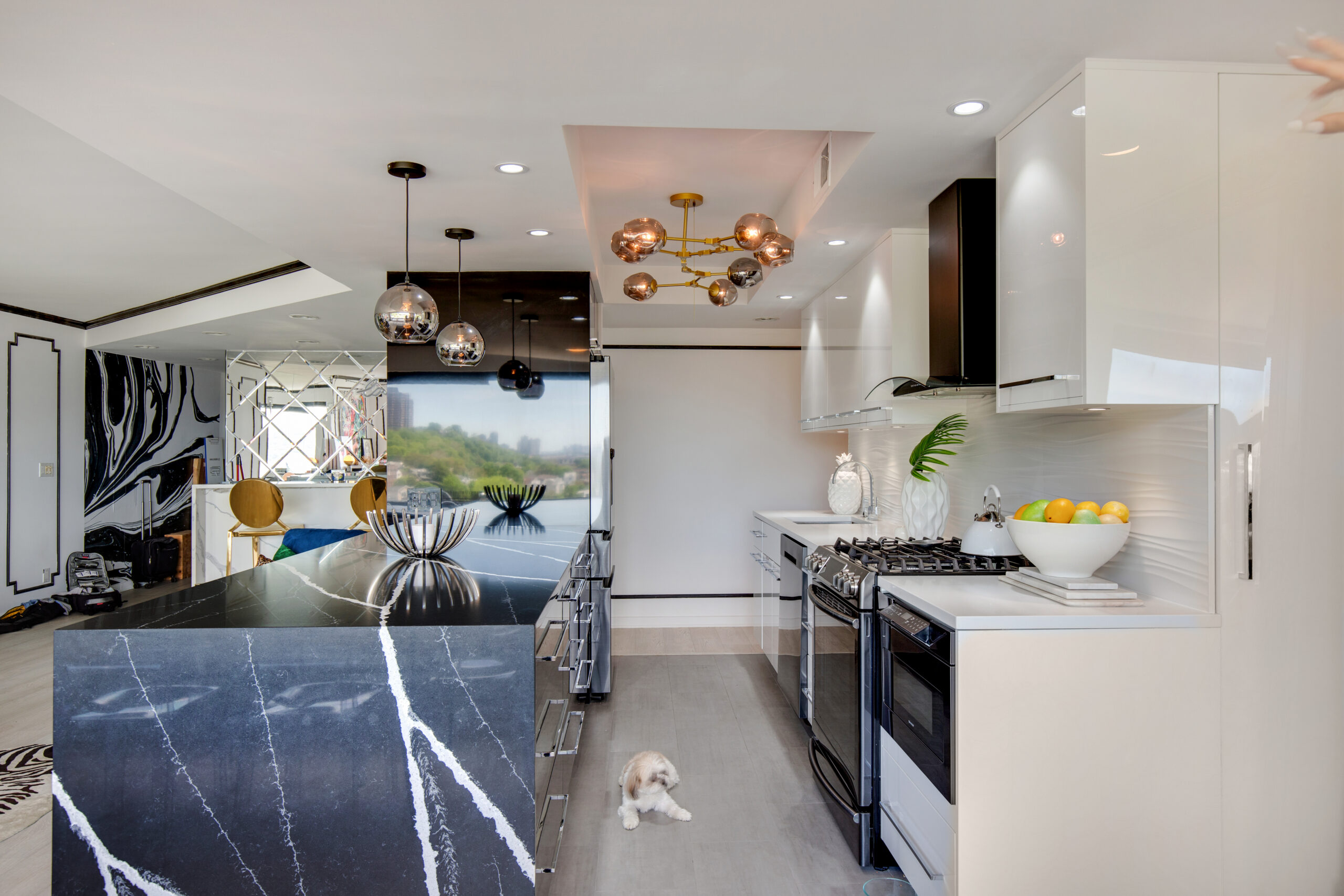 The Edgewater kitchen is open with a black waterfall island, white cabinets, sculptural lighting, and clear sight lines into the adjacent living room.