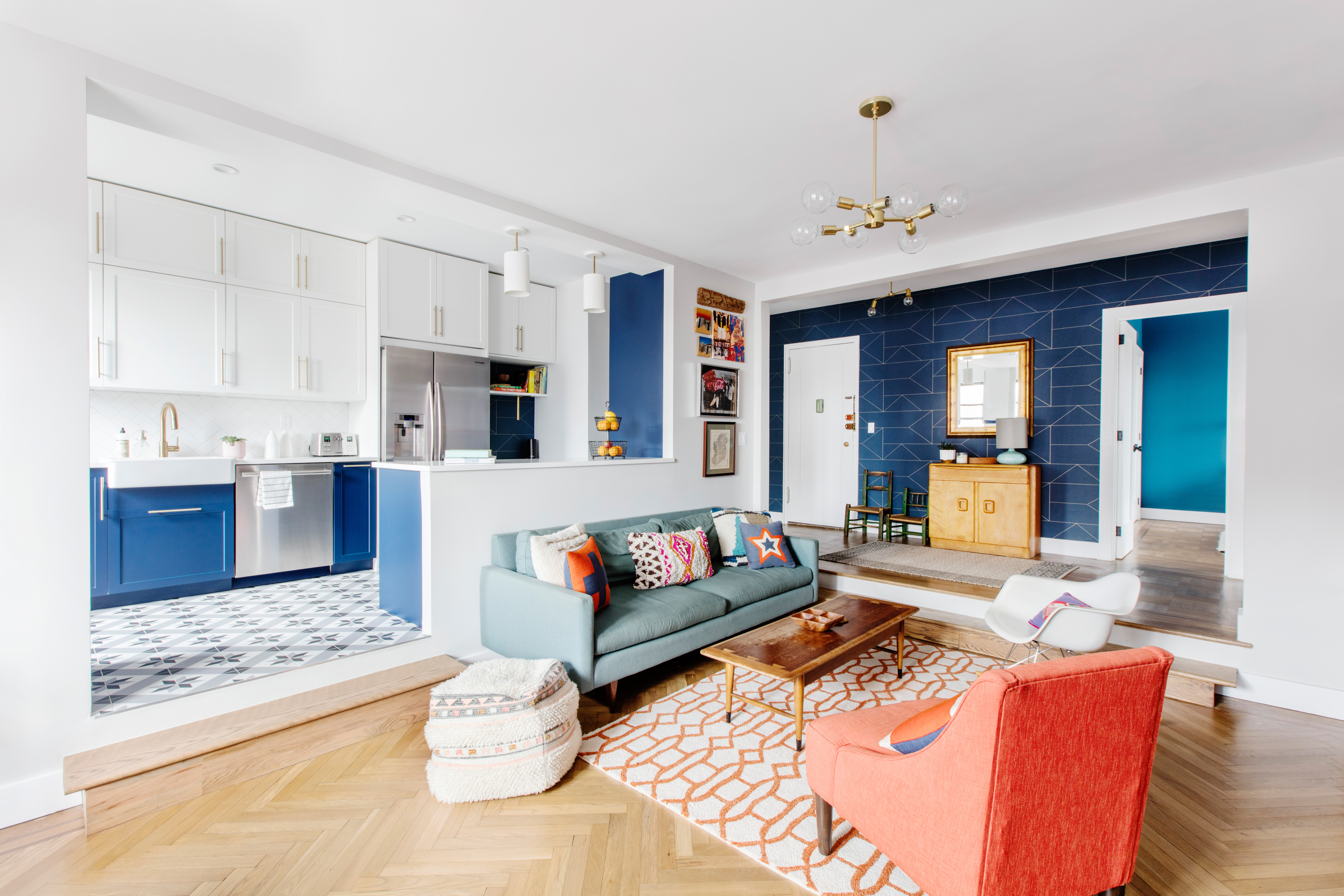 Refinished herringbone wood flooring, blue kitchen cabinets, patterned tiles, colorful seating, and brass lighting in this renovated Kensington apartment.