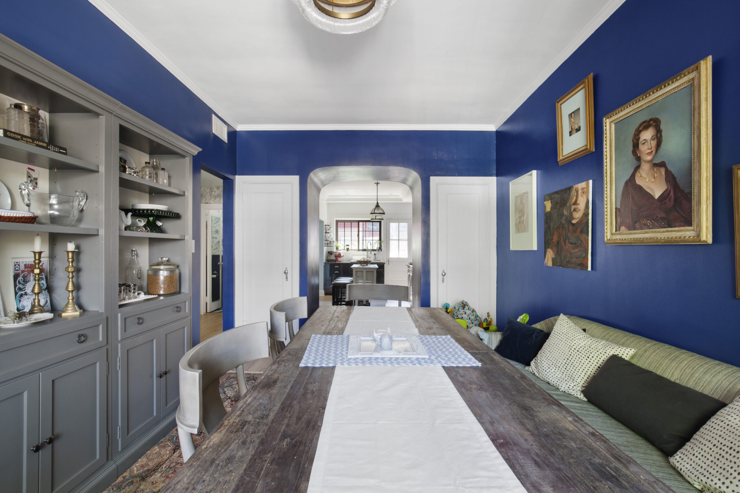 Kensington townhouse design with a preserved arched doorway, deep blue dining room walls, built-in storage, wood table, and a clear view to the kitchen.