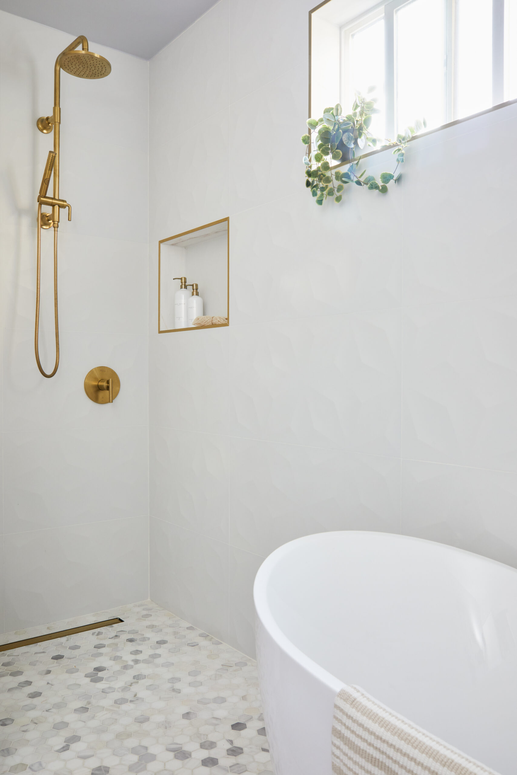 Los Angeles primary bathroom wet room pairs a freestanding tub with a brass rain shower, built-in niche, hex mosaic floor, and natural light.