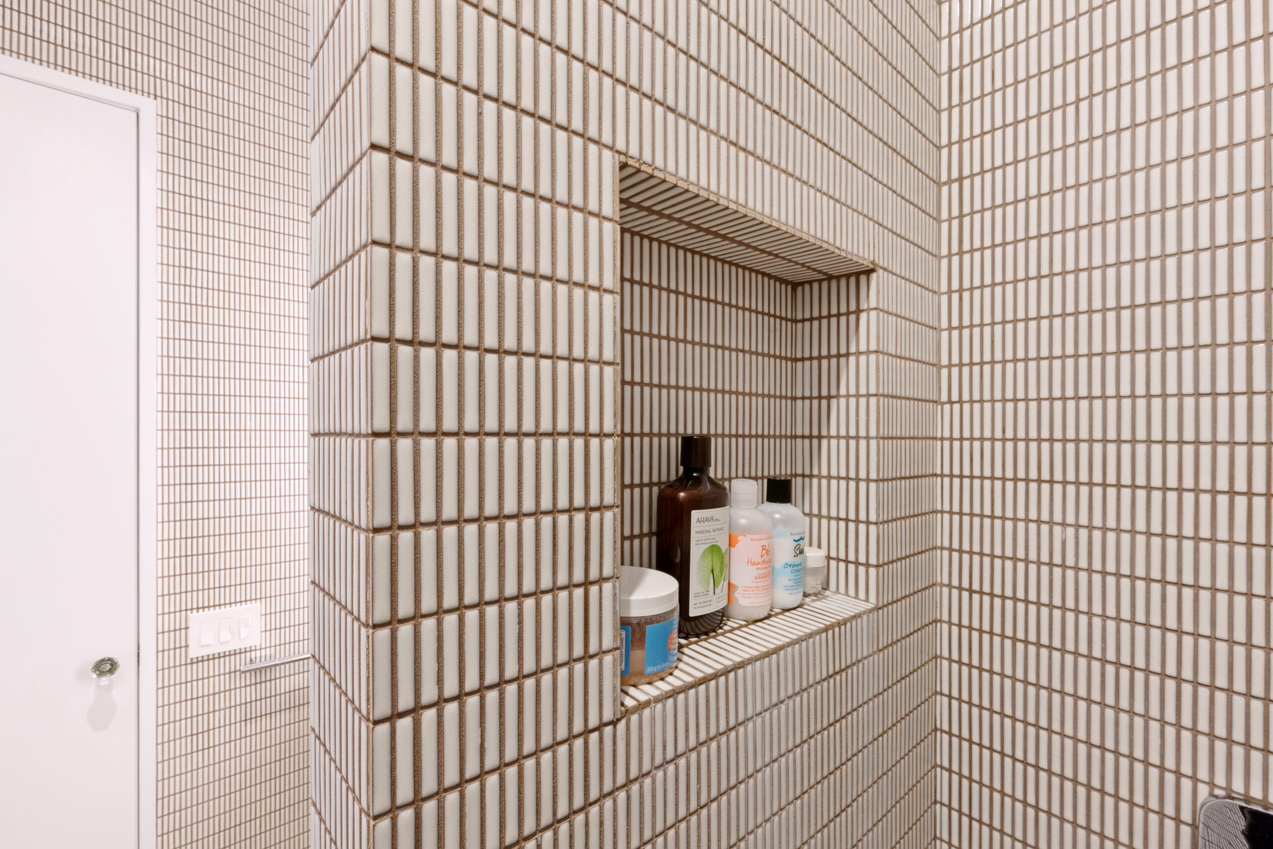 A recessed shower niche is built into a tiled wing wall, keeping bottles tucked from the main view while adding concealed storage in New York City.